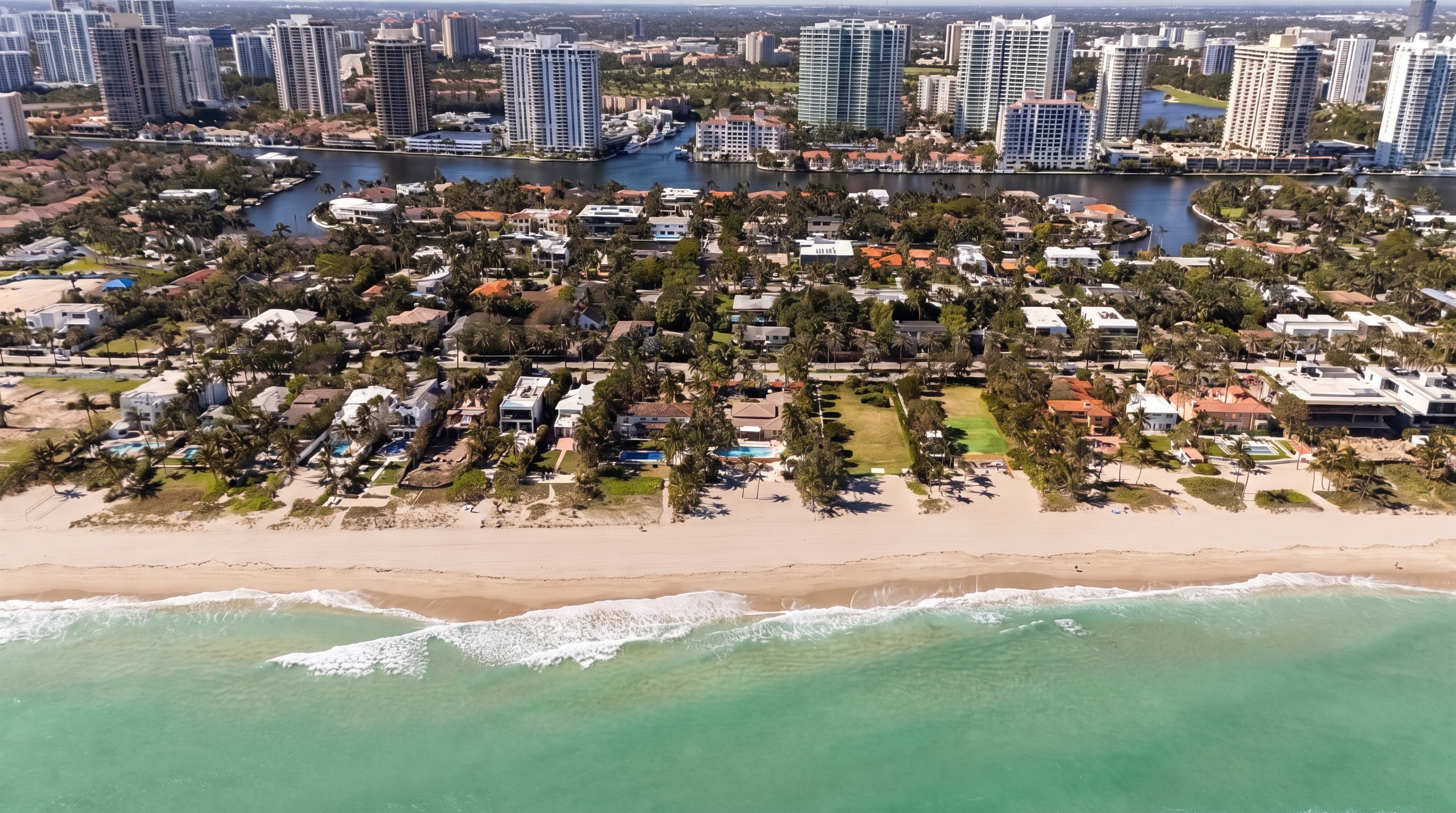 This high-altitude aerial view captures a prime beachfront property highlighted by a red outline, situated directly on the sandy coastline. The perspective showcases the home's proximity to the ocean, its private pool, and the surrounding lush tropical landscaping. In the background, a dense urban skyline of high-rise buildings and a calm waterway provide a striking contrast to the serene beach setting.