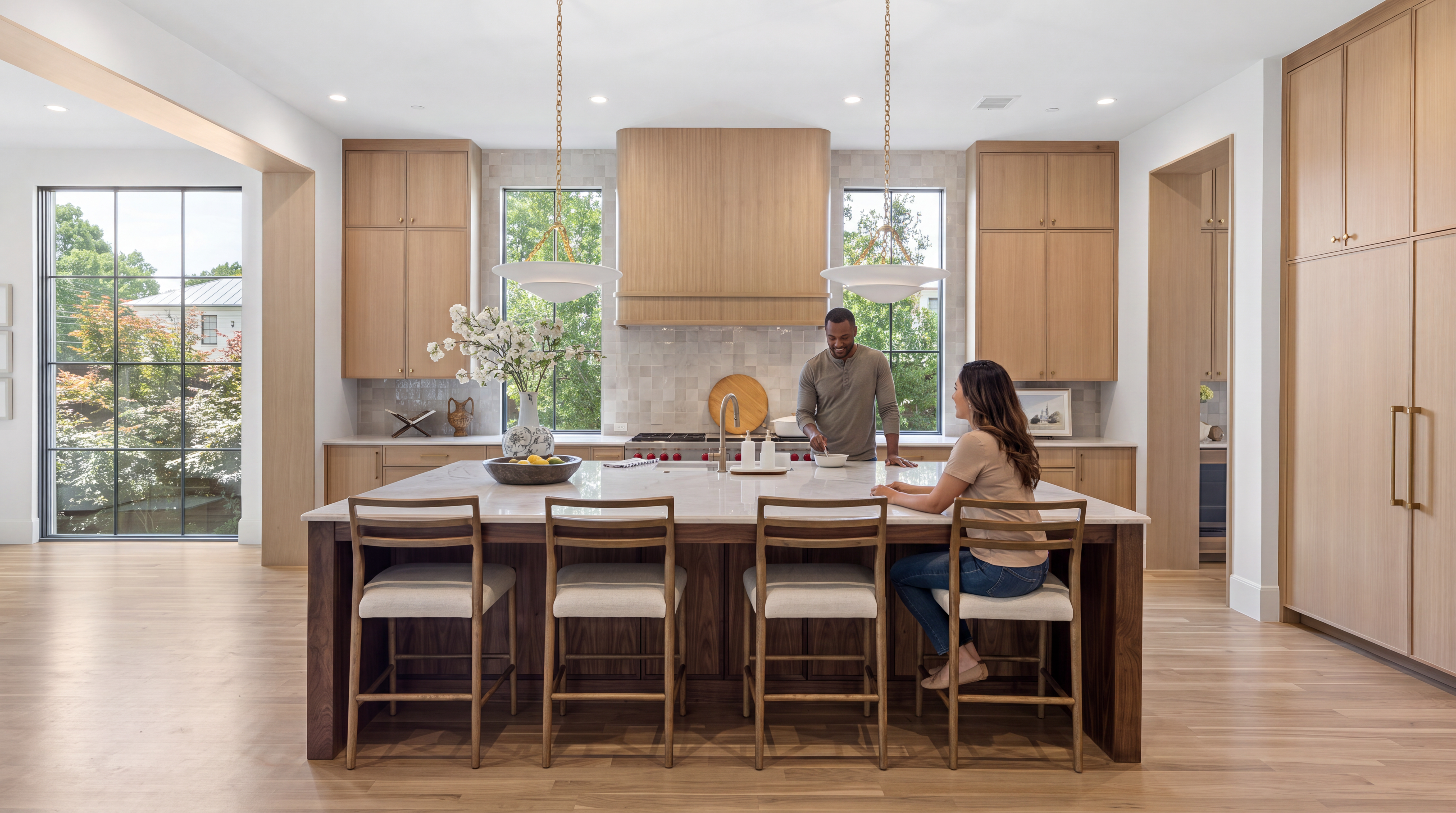 This modern, light-filled kitchen features warm natural wood cabinetry paired with a generous marble-topped island that serves as a central hub. It is equipped with high-end appliances, stylish pendant lighting, and large windows that provide abundant natural light and exterior views. The space exudes a luxury, contemporary feel, perfect for both functional cooking and social interaction.