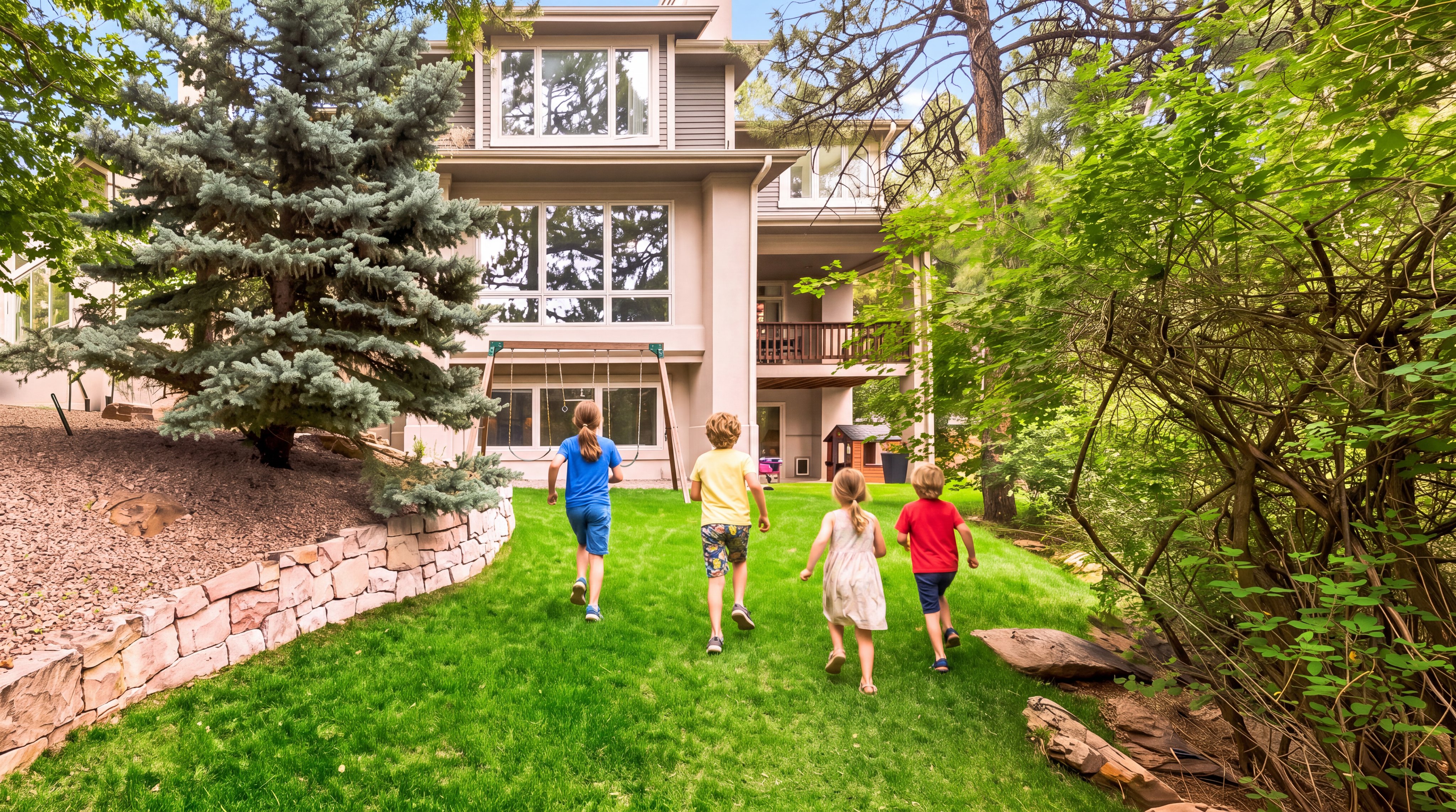 This image showcases a spacious backyard setting featuring a multi-level contemporary home with large glass windows and an attached wooden deck. The expansive, well-manicured lawn includes a children's playset and a small playhouse, making it an ideal family-oriented outdoor space. Lush surrounding trees and a decorative stone retaining wall enhance the private and natural feel of this property.