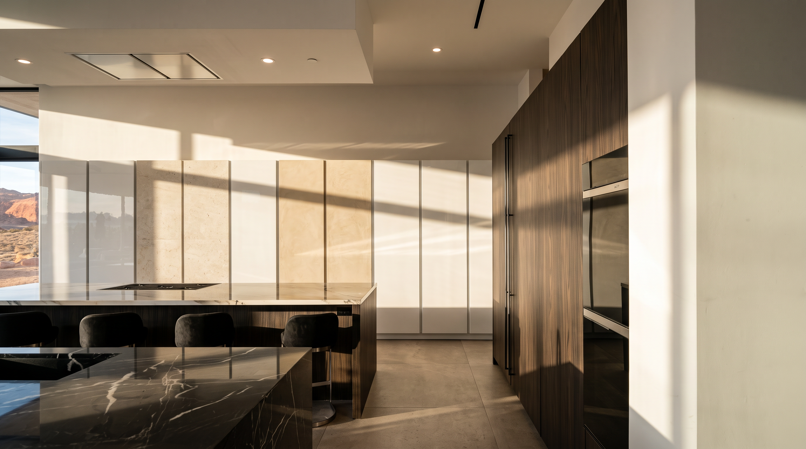 This modern, minimalist kitchen features a large island with a dark, patterned stone countertop and integrated seating. The space is defined by a striking contrast between the high-gloss white cabinetry lining the back wall and the dark, wood-paneled wall housing built-in appliances. The perspective is captured from a low angle, emphasizing the clean lines and the expansive, open-concept layout of the room.