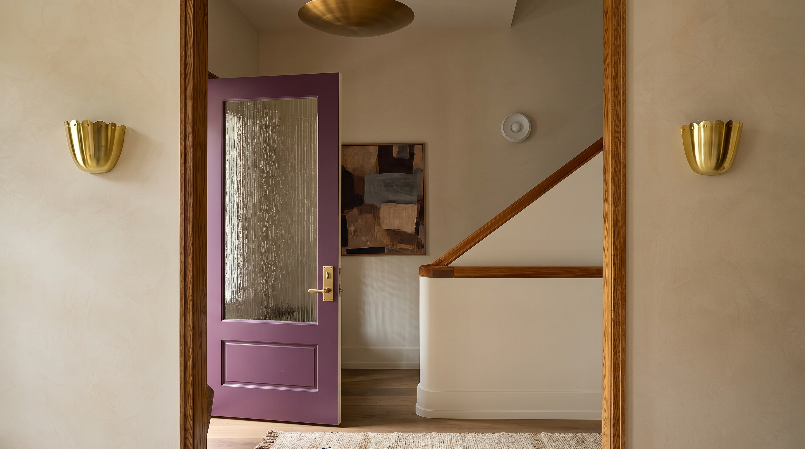 This interior view captures a transition space featuring a warm, wood-trimmed doorway that frames a view into a hallway with a staircase. The foreground is adorned with elegant gold wall sconces and a textured rug, while the background reveals a striking purple door and a piece of abstract art. The overall aesthetic is sophisticated and curated, blending modern textures with classic architectural details.