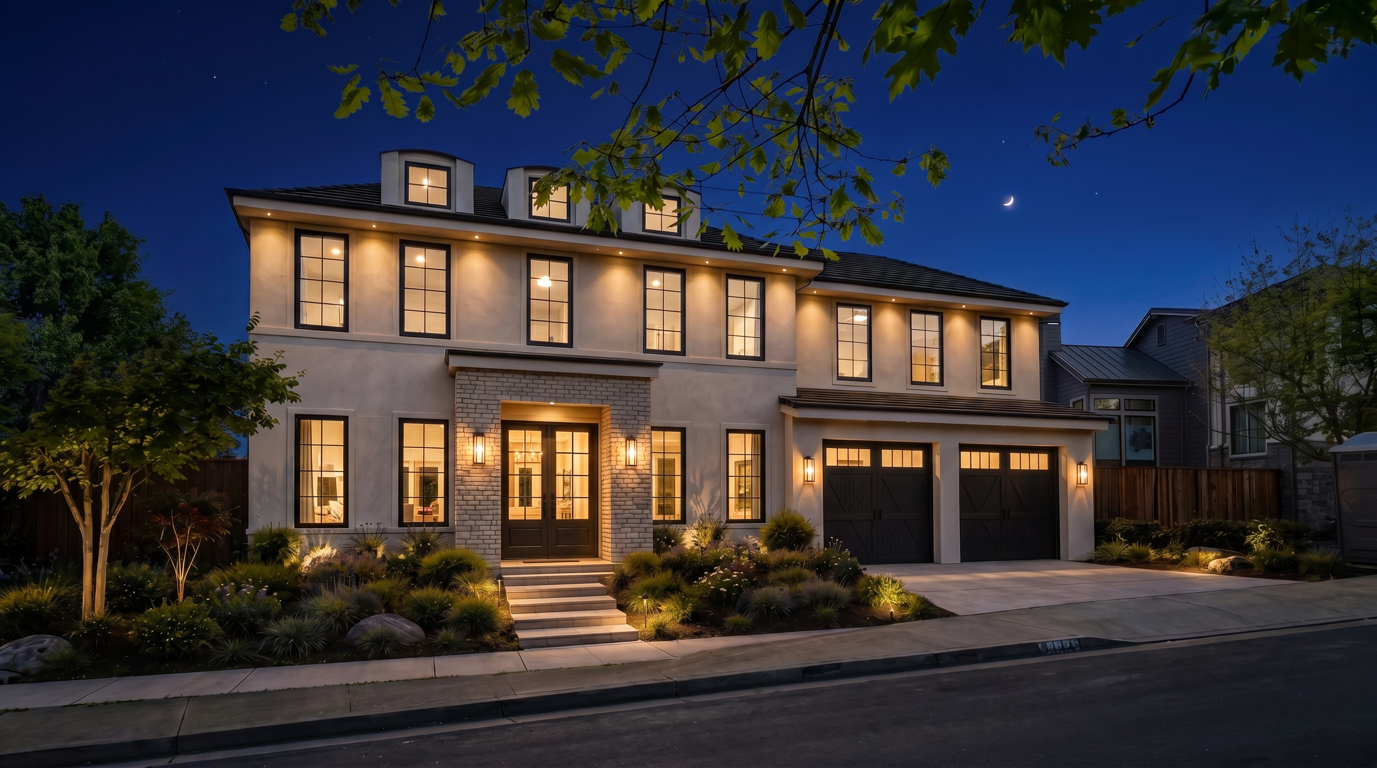 This modern, two-story residence features a sophisticated stucco and brick facade with large, dark-framed windows and a striking purple-leafed tree as a central focal point. The property includes a spacious two-car garage, an inviting elevated entryway with clean stone steps, and meticulously landscaped gardens in the front yard. Its contemporary aesthetic is enhanced by architectural details like the eyebrow dormers on the roof and a balanced, symmetrical design.