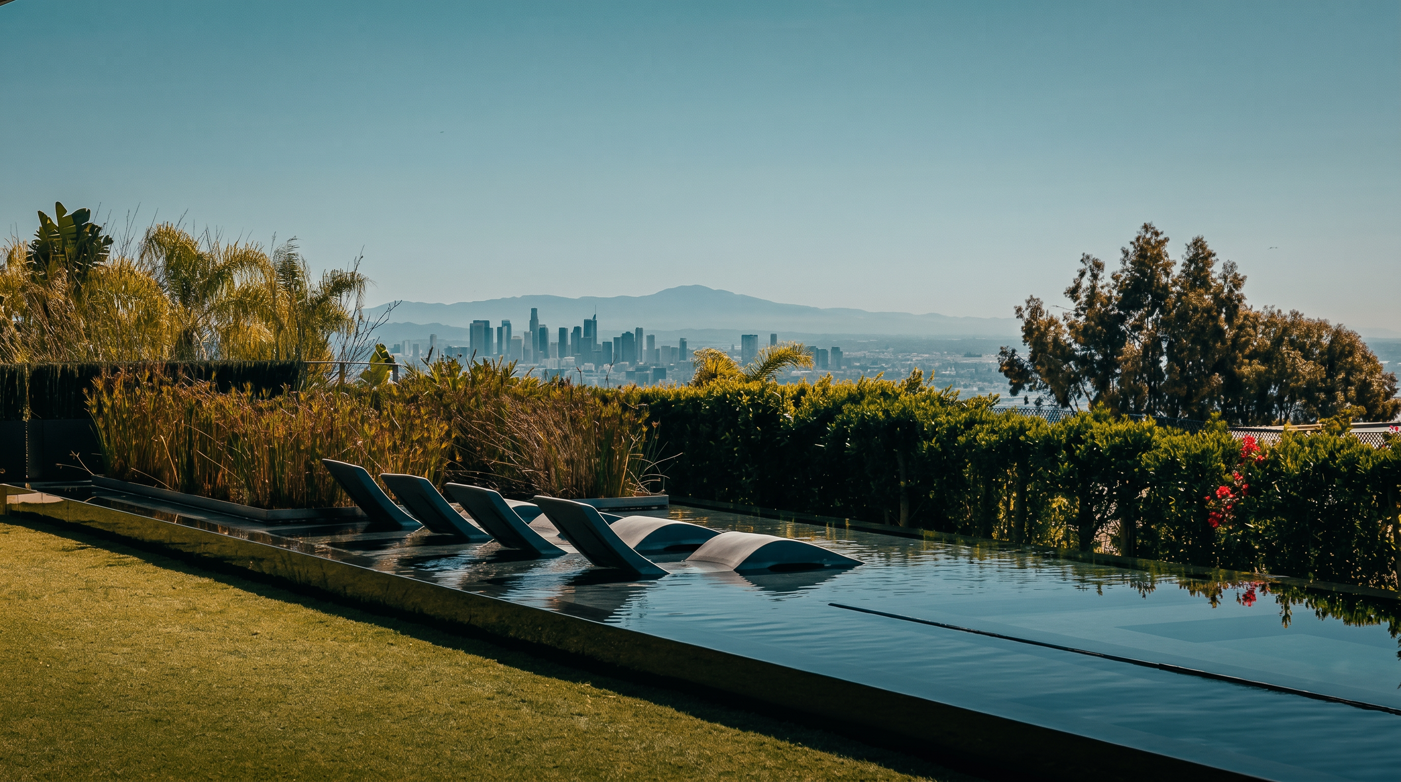 This stunning infinity-edge pool features submerged lounge chairs, creating a luxurious resort-like atmosphere. The pool overlooks a panoramic cityscape, framed by lush green hedges and a manicured lawn. The perspective captures the seamless transition between the private outdoor space and the expansive urban horizon.