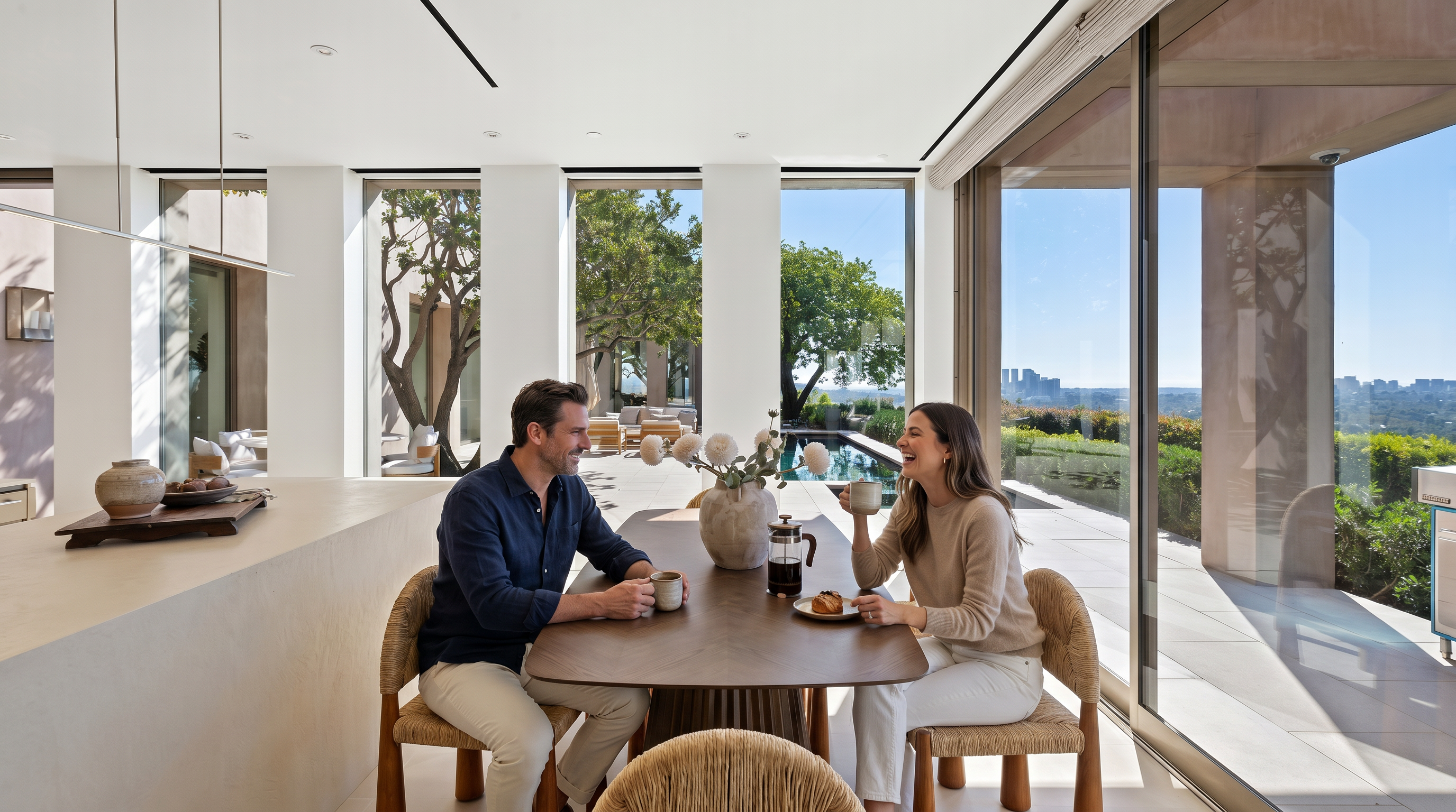 This elegant dining area seamlessly blends indoor and outdoor living with floor-to-ceiling glass walls that open to a scenic terrace and pool. The space features a minimalist, modern aesthetic with a dark wood dining table, woven chairs, and a sculptural vase centerpiece. The neutral color palette and clean lines create a sophisticated, airy atmosphere that highlights the expansive city views.