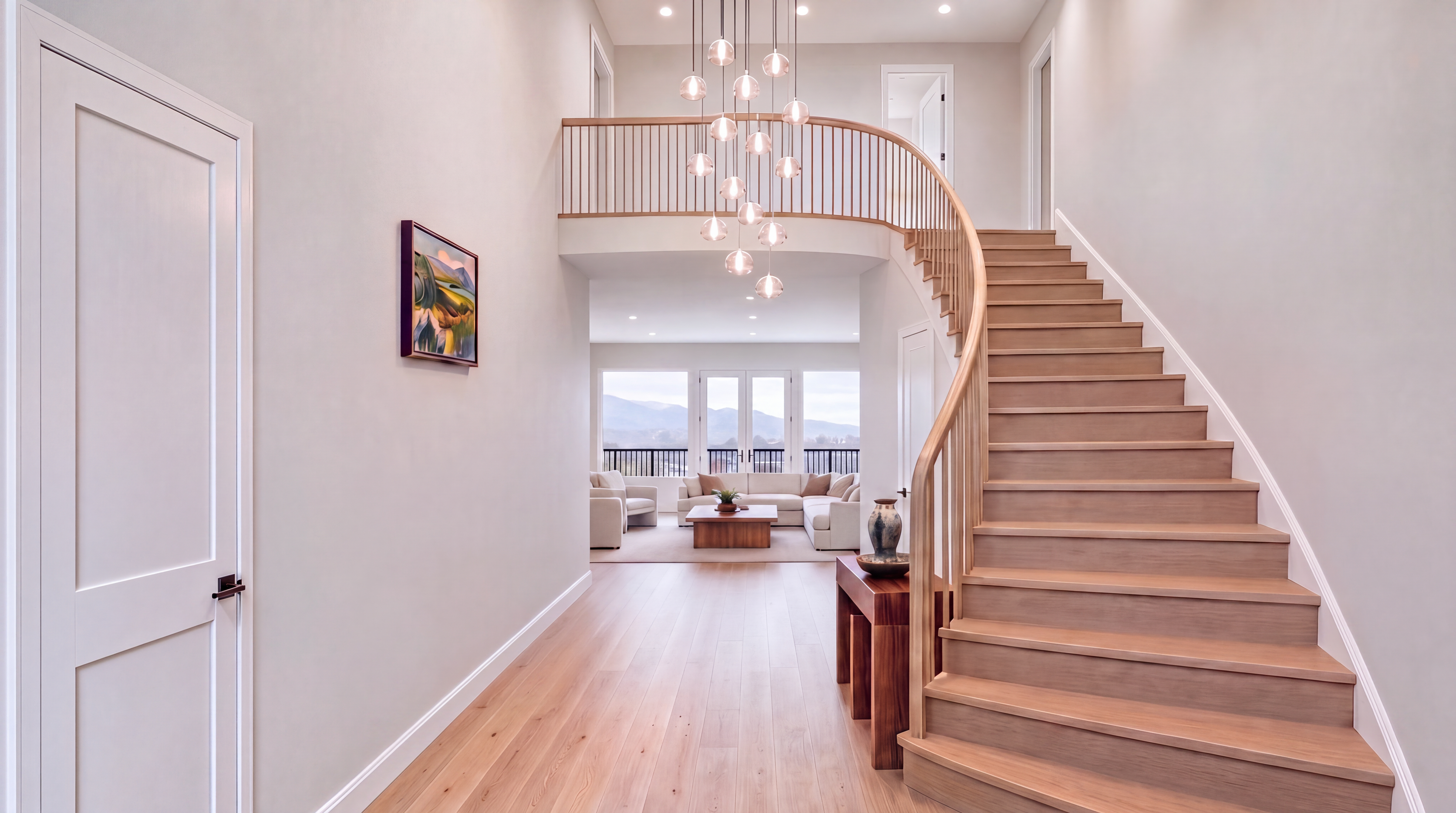 This grand entryway features a stunning curved wooden staircase and a contemporary multi-pendant chandelier that serves as a dramatic focal point. The open-concept design flows into a bright, airy living area with expansive windows that offer picturesque mountain views. The light wood flooring and neutral color palette contribute to a sophisticated, modern, and inviting atmosphere.