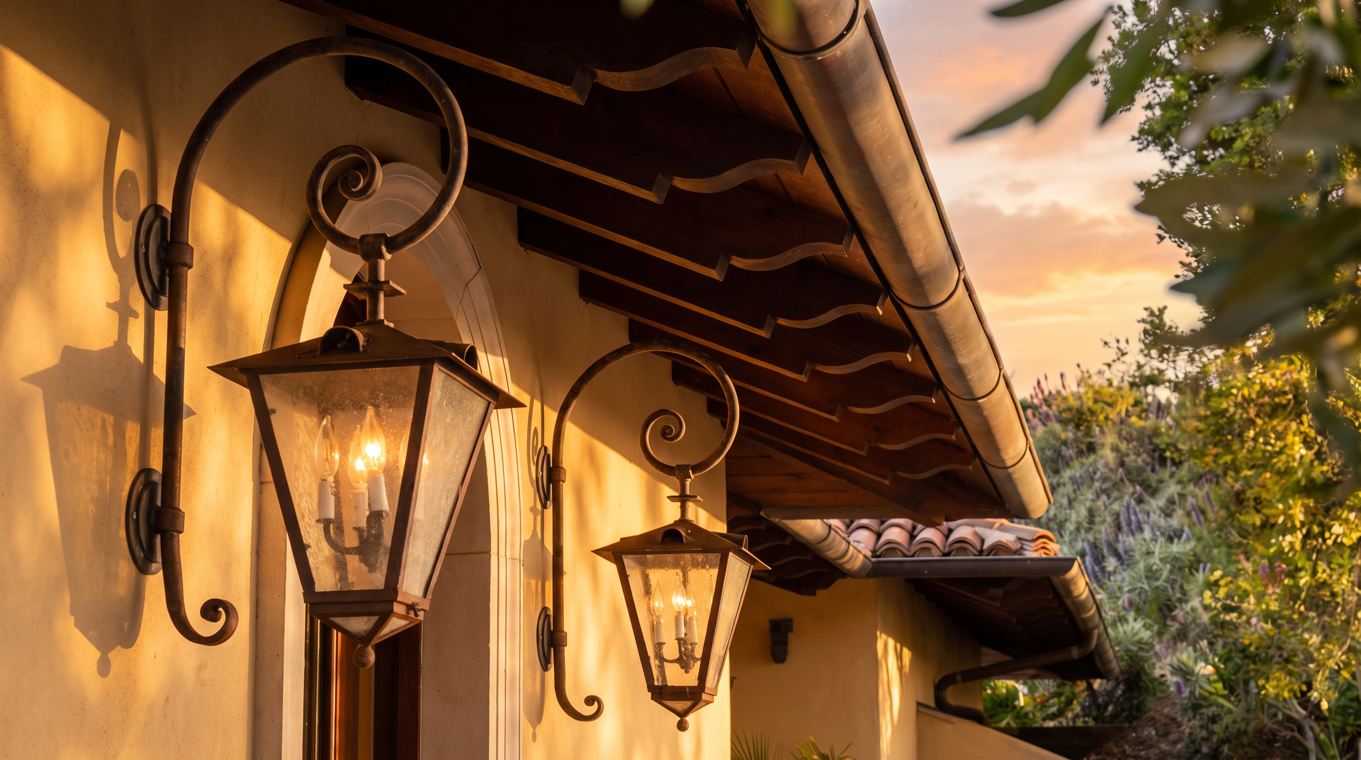 This close-up perspective highlights the elegant Mediterranean-style exterior of a home, focusing on two ornate, wrought-iron wall lanterns mounted against a warm, stucco-finished wall. The scene captures the intricate craftsmanship of the dark wood corbels supporting the overhanging roof eaves, which feature a classic terracotta tile roofline. The composition emphasizes the architectural texture and historical charm of the home's entryway.