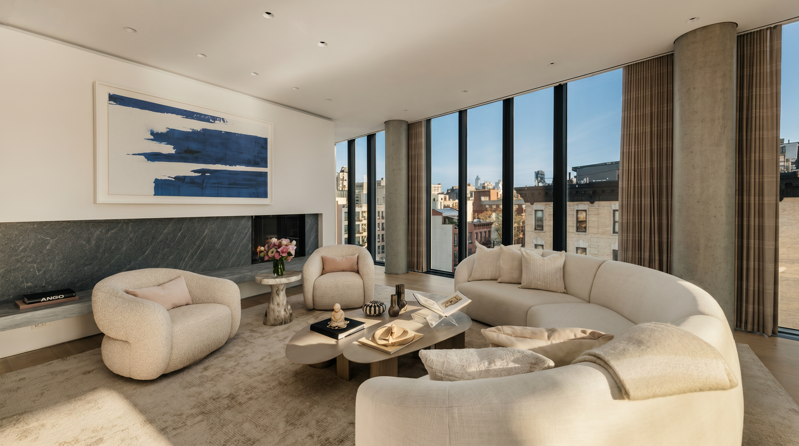 This sophisticated living room features a curved sofa and two plush armchairs arranged around a sculptural coffee table on a neutral area rug. A striking blue abstract painting hangs above a sleek, dark stone fireplace surround, while expansive floor-to-ceiling windows provide abundant natural light and urban views. The space is defined by its minimalist aesthetic, soft textures, and a neutral color palette that creates an airy, high-end atmosphere.