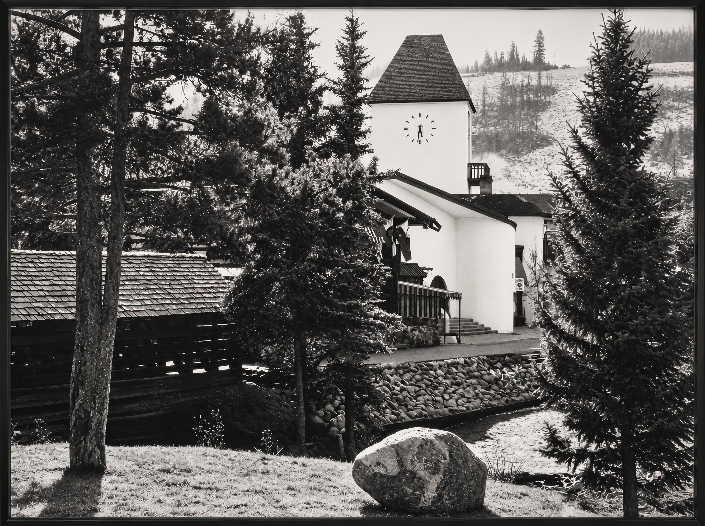This black and white image features a charming alpine-style building with a prominent clock tower, set amidst a scenic, landscaped outdoor space with lush evergreens and a rock-lined water feature. The scene highlights a peaceful courtyard or common area, likely serving as a central focal point for a community or resort development. Its rustic, picturesque aesthetic creates an inviting and serene atmosphere suitable for a real estate property highlight.