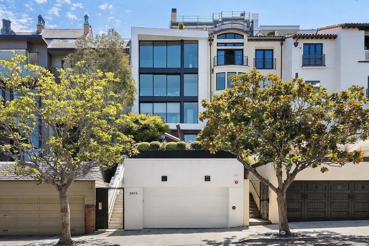 This front-facing view captures a modern, multi-story residence nestled between traditional architectural styles in an urban setting. The home features a prominent, multi-level glass facade that contrasts with the white stucco exterior and a wide, central garage door marked with the address 2833. Mature trees frame the property, adding a touch of greenery to the streetscape, while a set of stairs leads to an elevated entrance area.