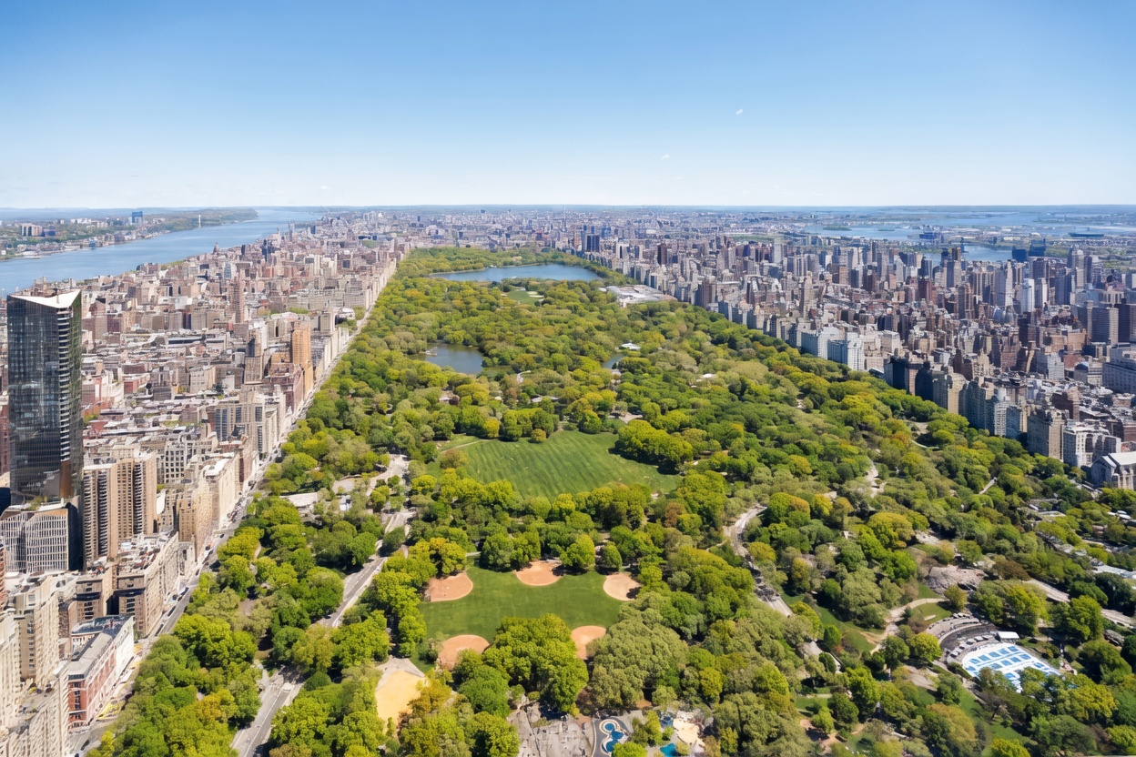 This high-altitude aerial perspective captures the vast expanse of Central Park in New York City, flanked by dense urban development on both sides. The lush green canopy of the park contrasts sharply with the surrounding grid of skyscrapers and city streets, stretching toward the horizon. The view provides a clear sense of the park's scale and its central role within the metropolitan landscape.