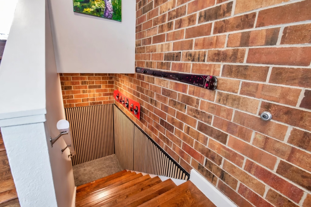 This staircase area features a unique design with wooden steps and a prominent brick feature wall. It includes creative decorative elements, such as a repurposed ski used as a wall-mounted hook rack, and wood slat paneling along the staircase side, providing a cozy, rustic, and playful aesthetic.