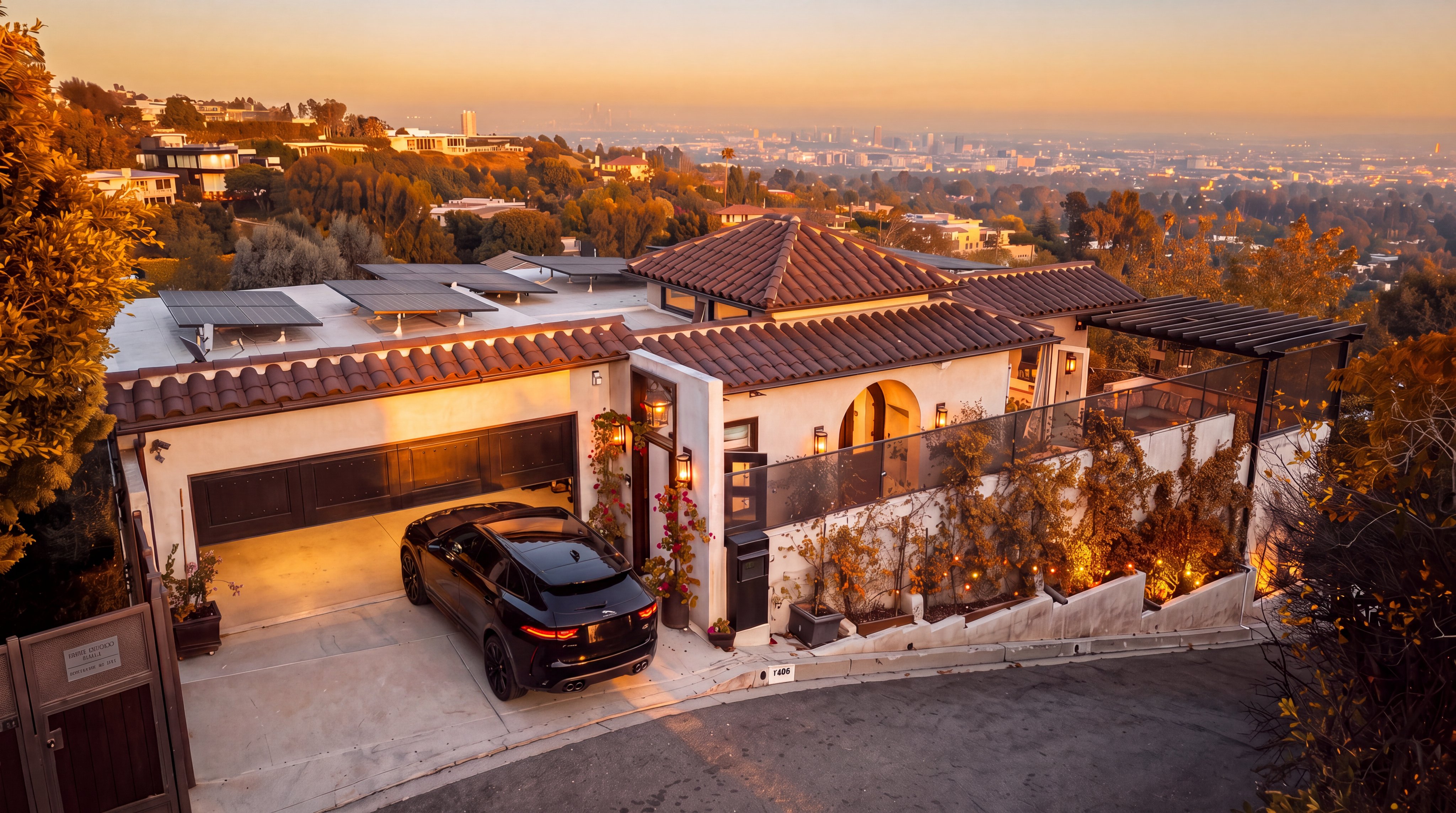 This stunning contemporary Mediterranean-style hillside home captures a breathtaking sunset view overlooking the city skyline. The property features a modern garage, solar panels, and a sleek, multi-level design that seamlessly integrates with its lush surroundings. The warm evening light enhances the elegant architecture and carefully curated landscaping, creating an inviting and luxurious atmosphere.