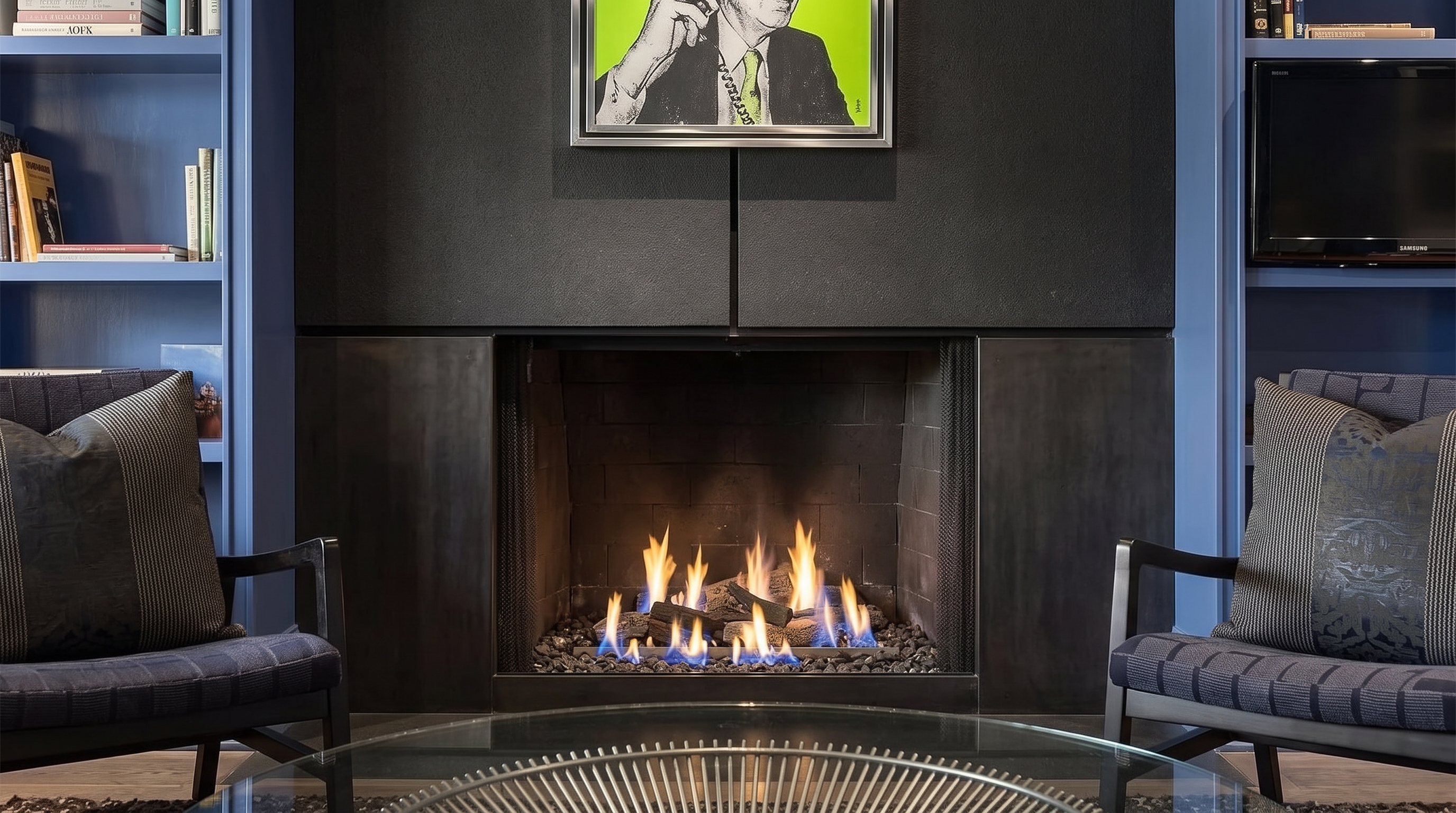 This sophisticated living room features a striking, dark-finished fireplace installation as its central focus, accented by a contemporary artwork above. The space is anchored by blue-toned armchairs and flanked by built-in shelving units, creating a balanced and refined seating area. The combination of industrial dark metal elements and modern decor provides a stylish, high-end ambiance.