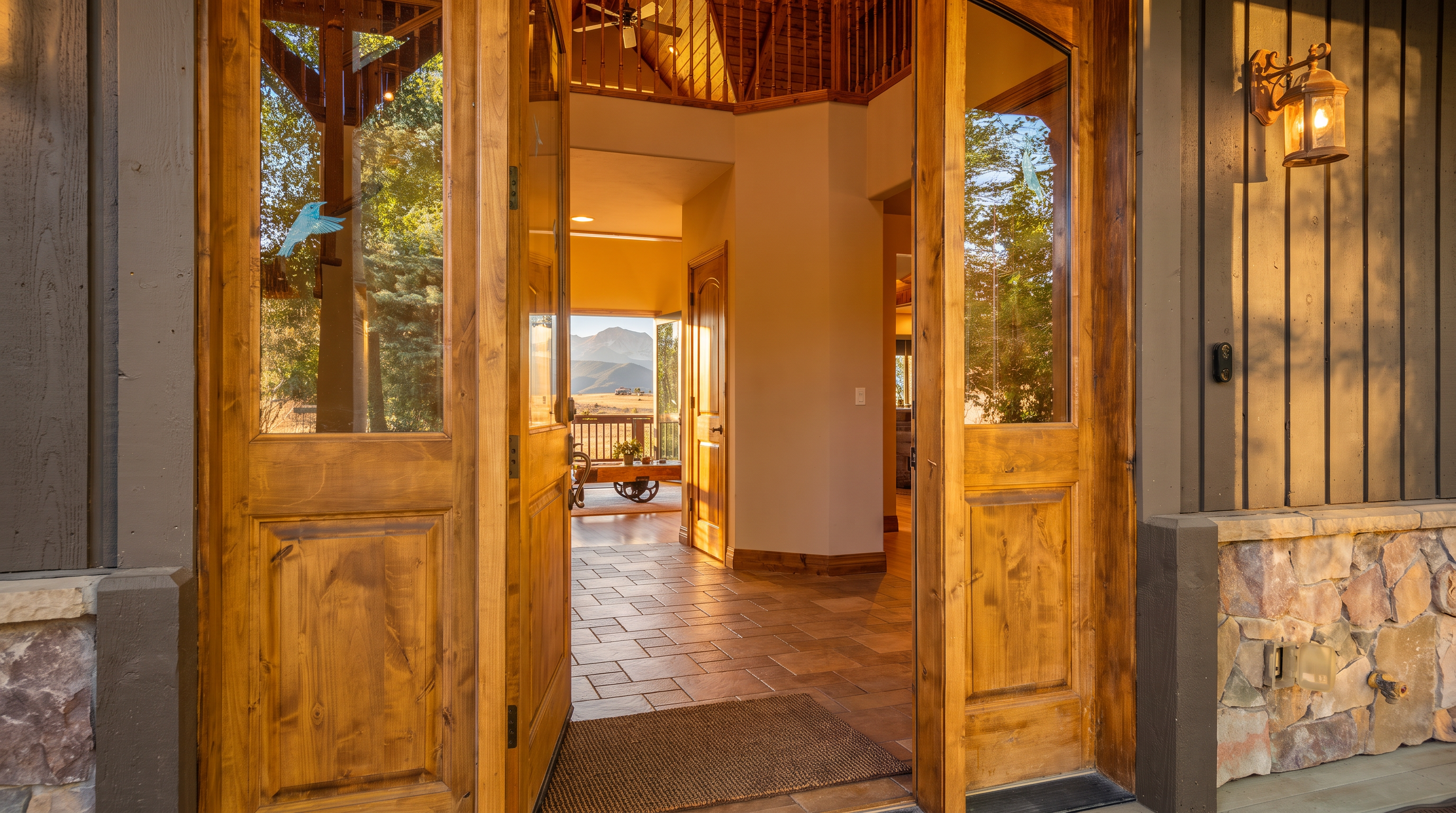 This image shows a welcoming entryway looking from the covered porch into the warm, inviting interior of a rustic-style home. The natural wood doors, tiled floors, and the stunning mountain view framed by the doorway highlight the property's seamless blend between elegant architecture and scenic outdoor beauty.