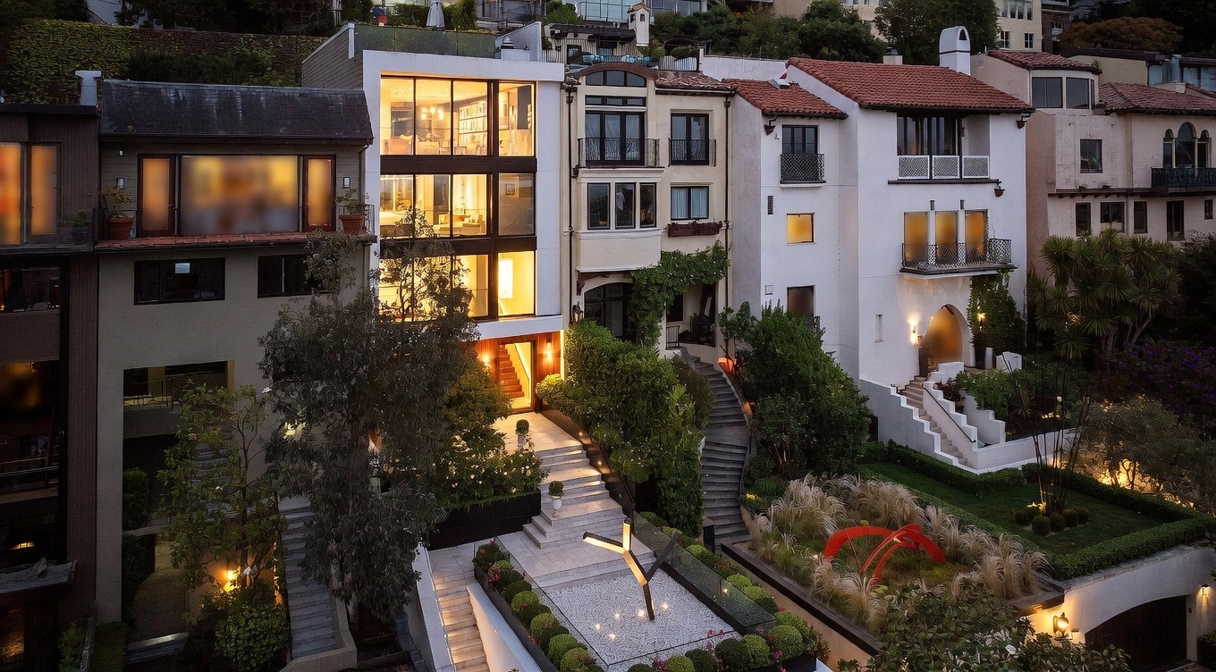 This elevated perspective captures a multi-level residential property featuring a striking modern home with large glass windows alongside more traditional architectural styles. The scene highlights a tiered landscape design with stone staircases, manicured hedges, and a sculptural art piece in the foreground. The warm glow from the interior lighting creates an inviting atmosphere against the twilight sky.