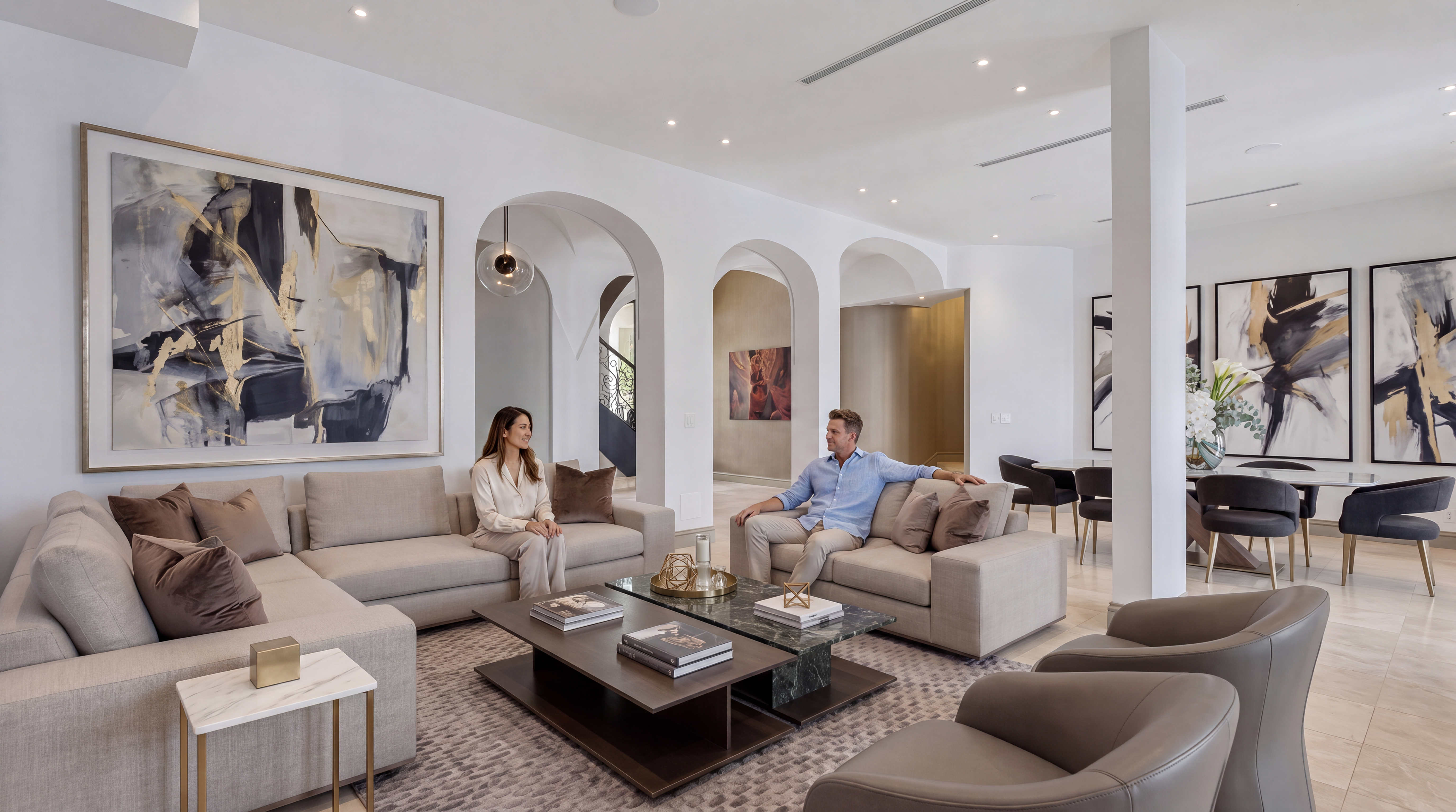 This spacious and elegant living room features a contemporary open-concept design with neutral-toned soft furnishings and a sophisticated earth-toned color palette. It is highlighted by architectural arched thresholds, large-scale abstract artwork, and premium finishes that create a luxurious, airy atmosphere. The space is well-integrated with a dining area, making it ideal for both entertaining and refined daily living.