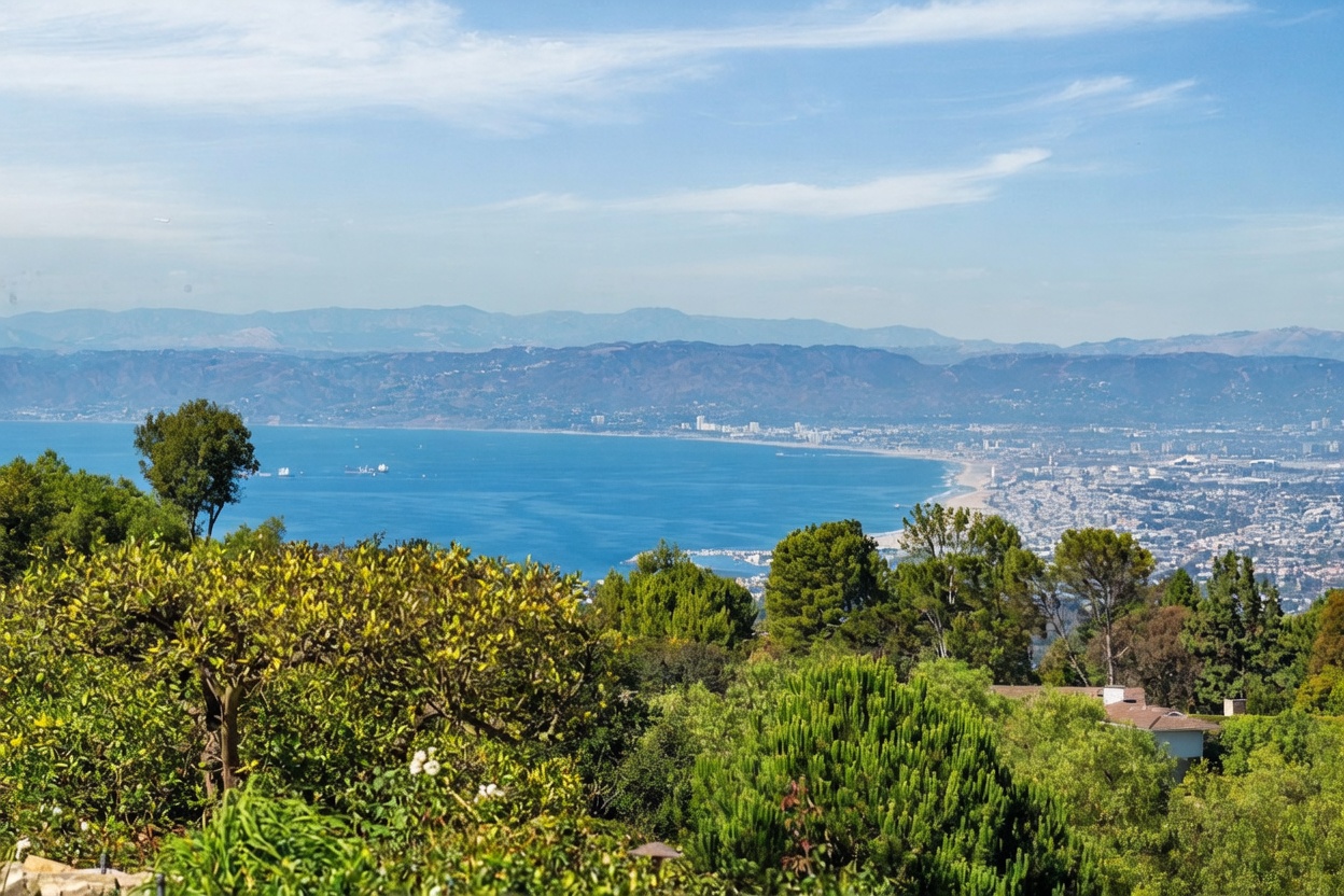 This elevated outdoor perspective captures a sweeping, panoramic view of a coastal bay and the surrounding city landscape. In the foreground, lush green trees and dense foliage frame the scene, providing a natural, serene setting. The expansive blue water stretches toward distant mountains, creating a picturesque and tranquil atmosphere ideal for a scenic property.
