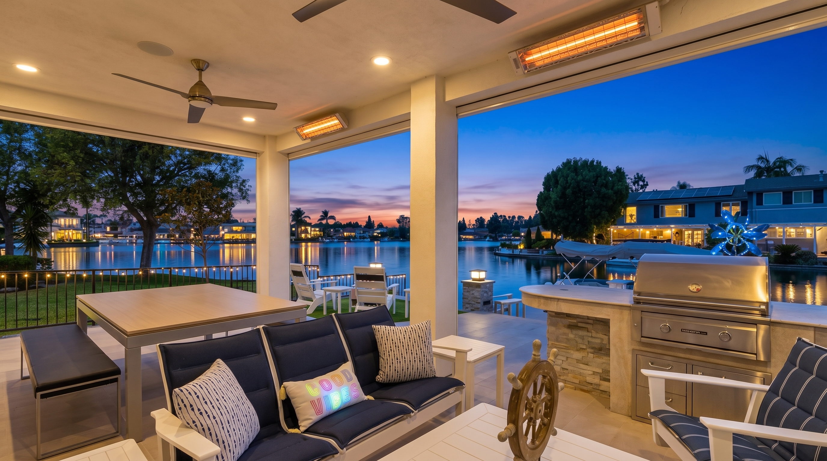 This spacious covered patio offers a luxurious outdoor living experience with direct views of a tranquil waterfront. The space is well-appointed with comfortable navy blue seating, a dining area, and a fully equipped outdoor kitchen, making it perfect for entertaining. The modern design and open-air layout create an inviting, seamless transition between the indoor comfort and the scenic natural surroundings.