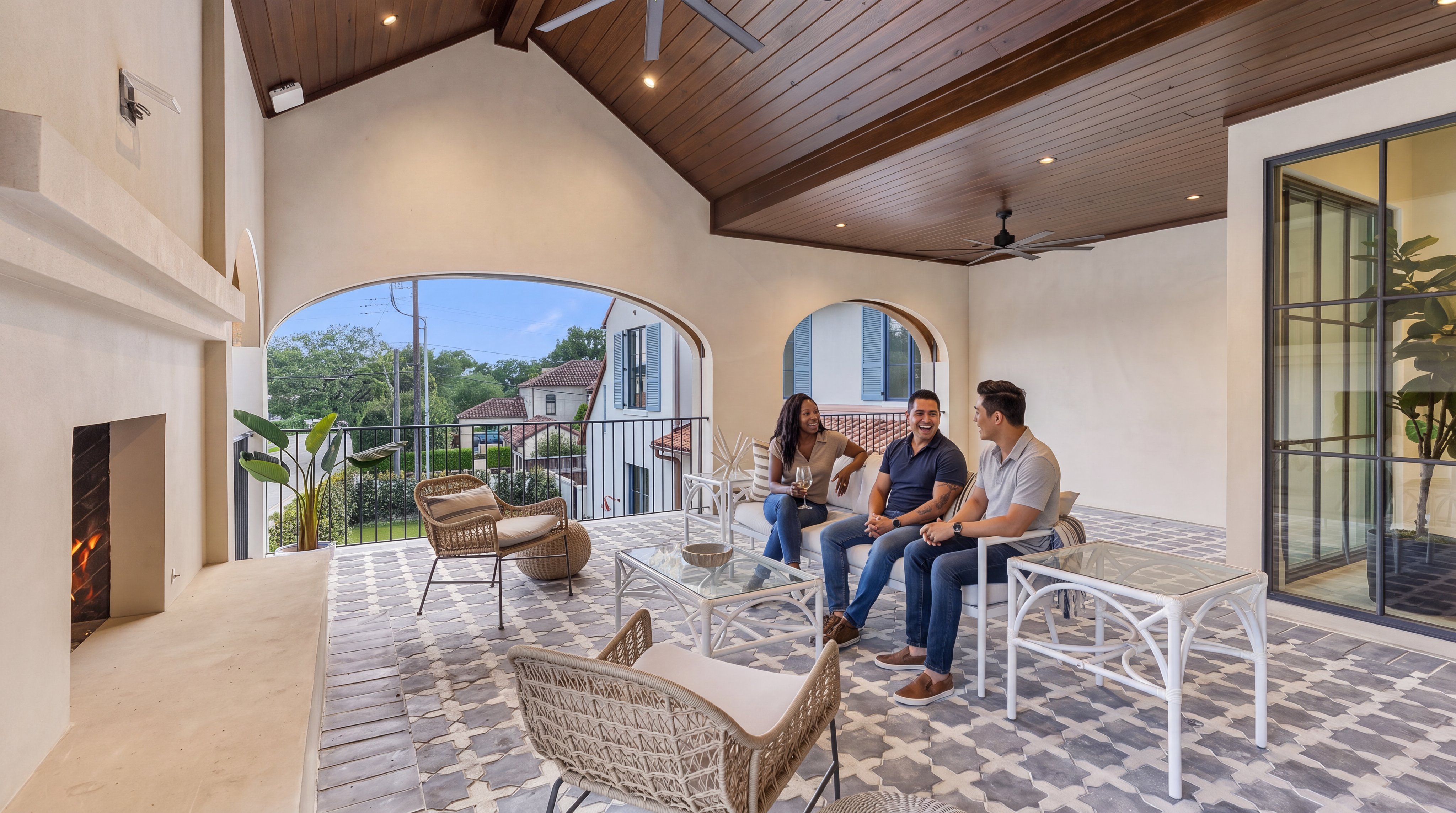 This luxurious covered terrace features a stunning vaulted wood ceiling and a sophisticated outdoor fireplace, creating an inviting space for relaxation. The area is elegantly furnished with comfortable seating, a stylish coffee table, and patterned floor tiles, all overlooking a quiet residential neighborhood. Its open-air design and high-end aesthetic make it a premier feature for outdoor entertaining.