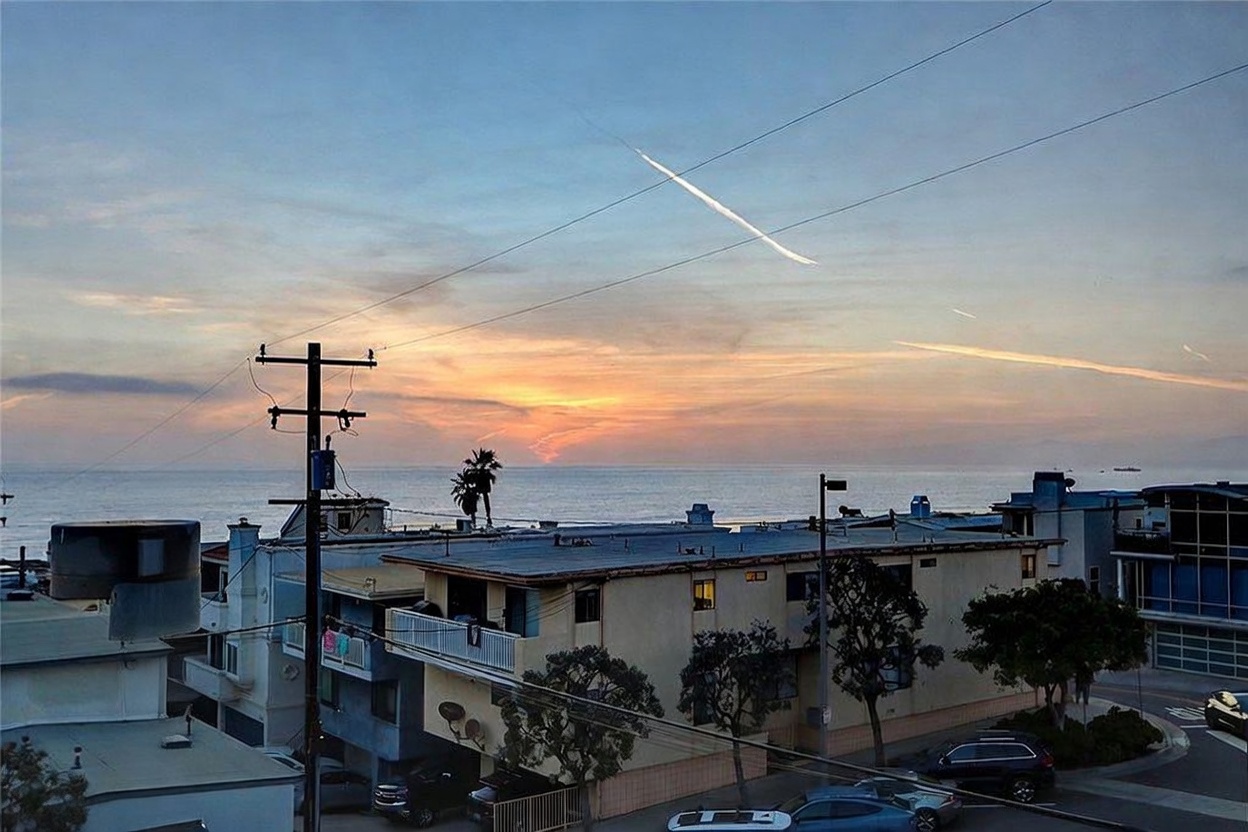 This elevated perspective captures a scenic coastal view at sunset, looking out over a multi-story residential building toward the ocean. The composition features a prominent utility pole in the foreground, with the soft, warm hues of the twilight sky reflecting over the water. The scene highlights the property's proximity to the coast and its neighborhood setting.