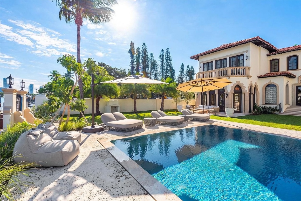 This luxurious Mediterranean-style estate features a pristine swimming pool set against a lush, manicured lawn and a multi-story residence. The outdoor living area is equipped with multiple lounge chairs, large umbrellas for shade, and a stone-paved deck, creating an inviting space for relaxation. The perspective captures the bright, sunny atmosphere of the property, highlighting the seamless transition between the elegant home architecture and the private backyard oasis.