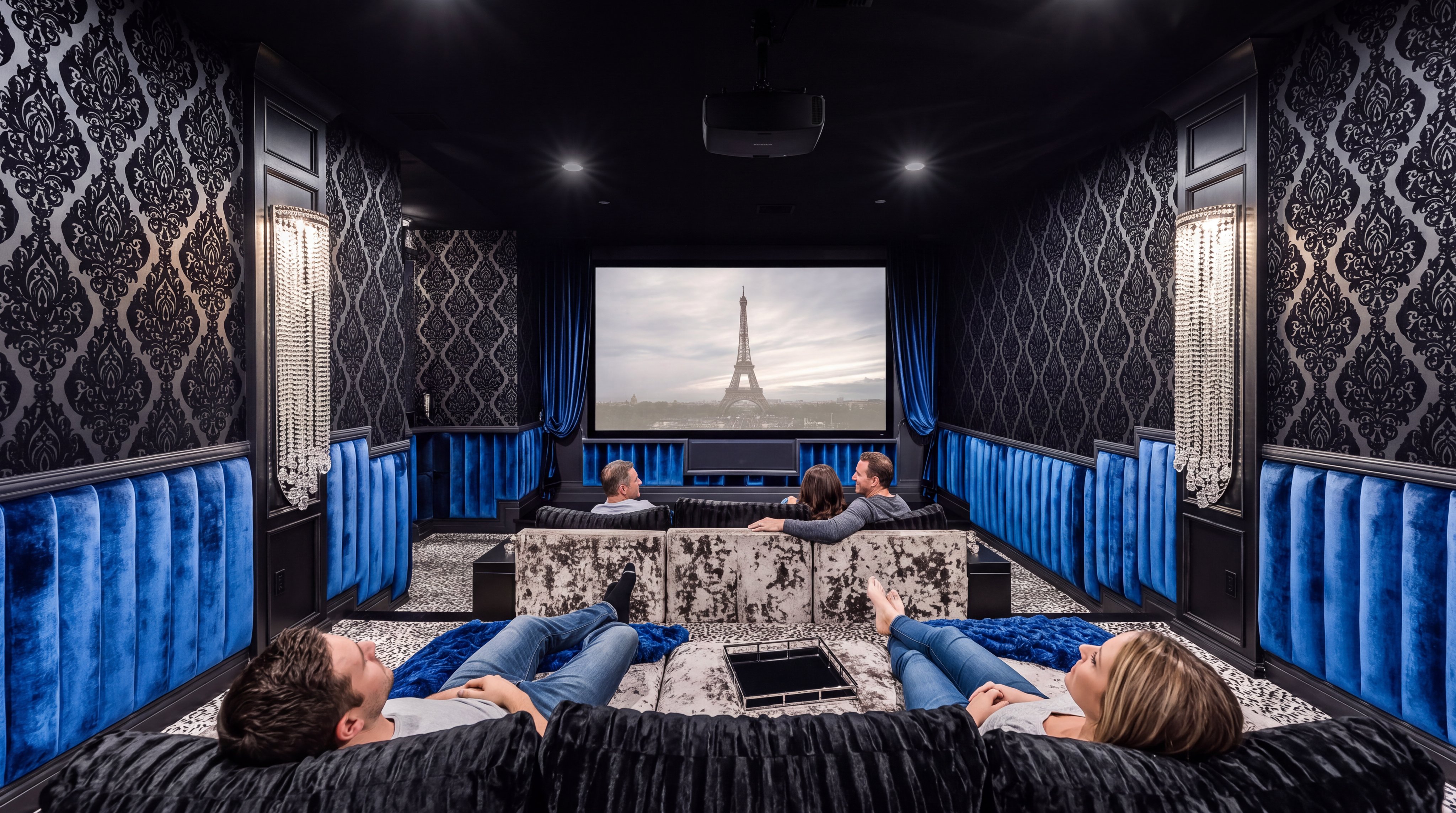This luxurious home theater features dramatic, opulent design with dark damask wallpaper, deep blue velvet wall panels, and crystal chandelier-style wall sconces. The room is tiered for optimal viewing, including a plush, oversized seating area in the foreground and a second row of seats facing a large projector screen displaying a scenic view of the Eiffel Tower. The overall impression is one of sophistication and an elevated cinematic experience, perfect for high-end home entertainment.