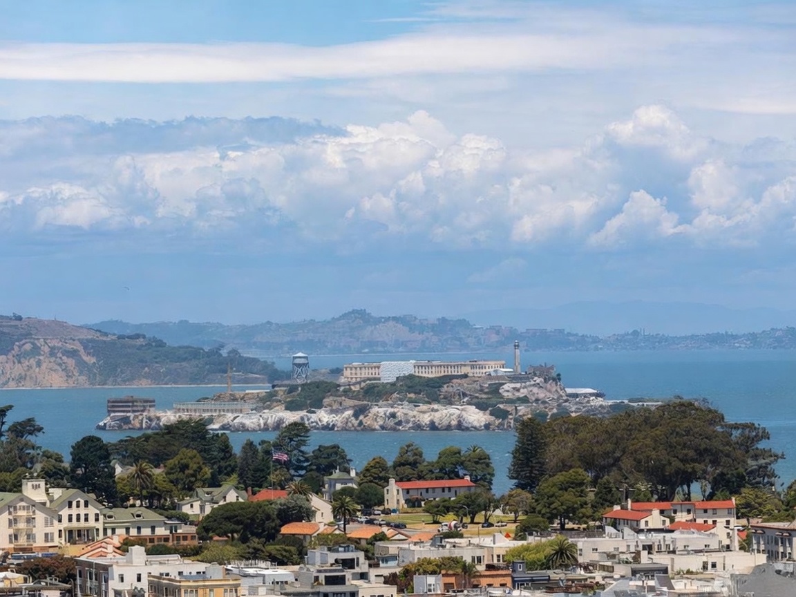 This elevated, wide-angle perspective captures a scenic urban landscape overlooking the San Francisco Bay, with the iconic Alcatraz Island prominently featured in the center. The foreground showcases a dense residential neighborhood characterized by traditional architecture, mature trees, and terracotta-tiled roofs. The composition provides a cinematic sense of scale, highlighting the property's proximity to historic landmarks and the expansive coastal environment.
