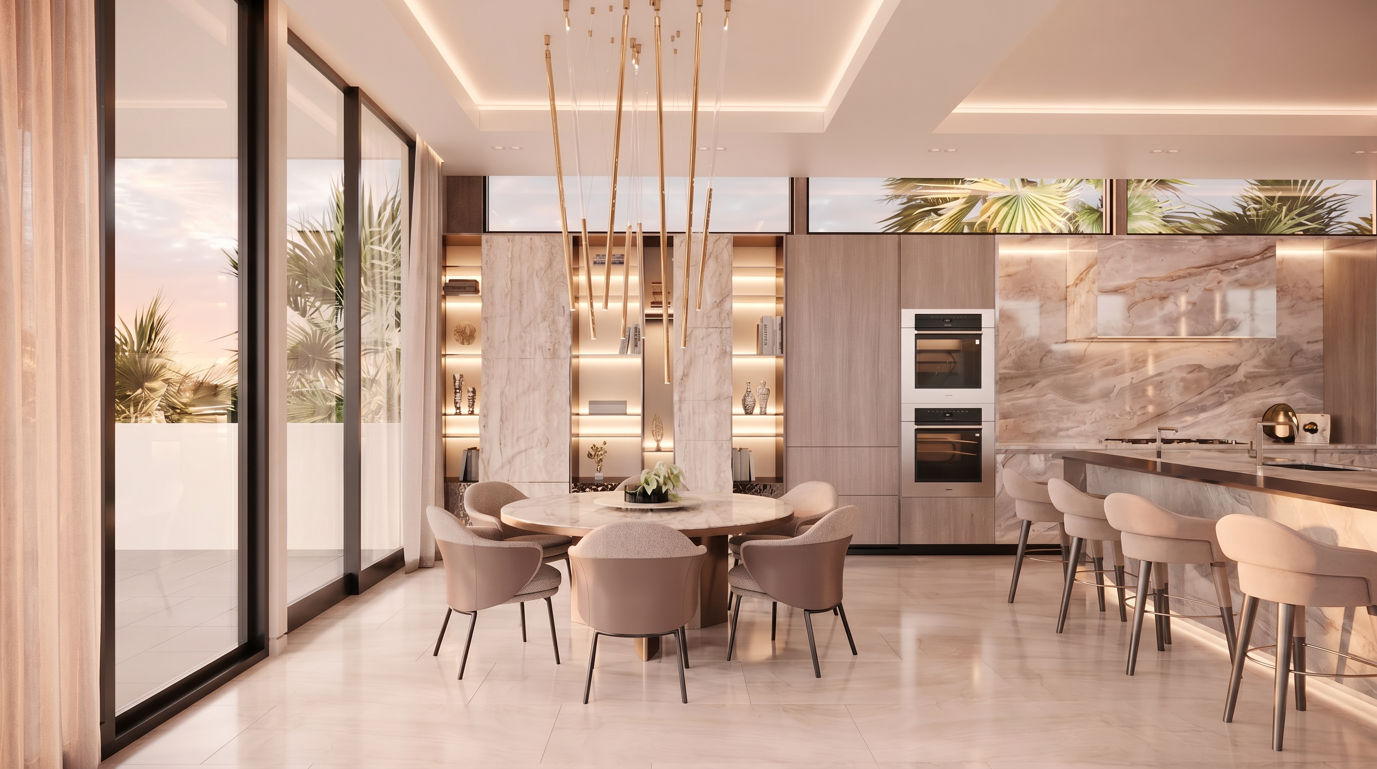 This sophisticated open-concept kitchen and dining area features a central round stone-topped table surrounded by modern upholstered chairs under a striking, multi-pendant gold light fixture. The space is anchored by a wall of integrated cabinetry, a double wall oven, and a stone-clad island with bar seating, all complemented by illuminated shelving units. Large glass sliding doors provide an expansive view of the outdoors, creating a seamless transition between the refined interior and the exterior environment.