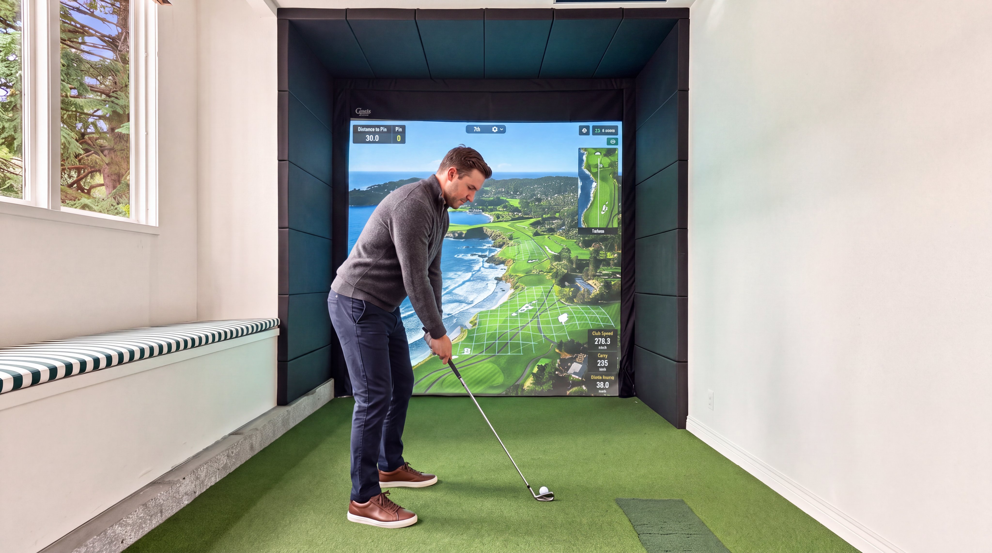 This interior space features a professional-grade indoor golf simulator, complete with a high-definition projection screen and a synthetic putting green surface. The room is designed with acoustic-style wall paneling around the simulator and built-in bench seating along the windowed wall, offering a luxurious recreation area perfect for leisure or training. The bright, clean aesthetic makes it an attractive and functional amenity for a high-end home.