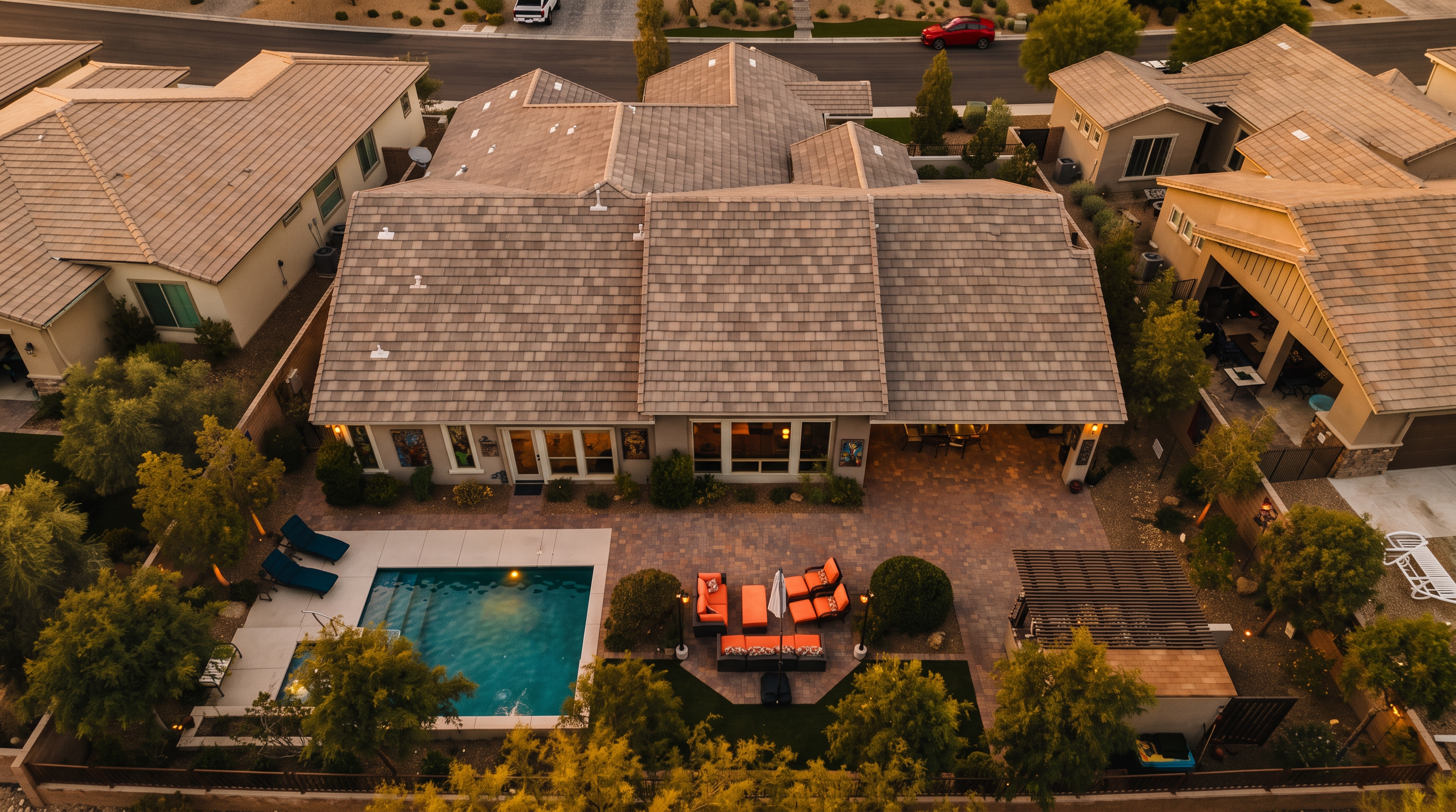 This high-angle aerial view showcases a modern single-story residence with an extensive backyard, highlighting a pristine swimming pool, a dedicated spa, and a spacious paver patio. The outdoor living area is well-equipped for entertaining, featuring comfortable lounge seating and a pergola-covered outdoor kitchen space. The property is neatly landscaped with lush greenery and surrounded by privacy walls, creating an inviting and well-maintained suburban oasis.