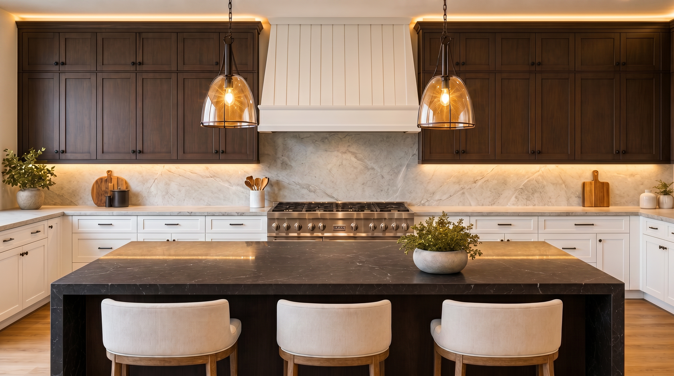 This sophisticated kitchen features dark wood cabinetry, a large central island with a dramatic dark stone countertop, and premium stainless steel appliances. A crisp white range hood serves as the focal point above the professional-grade stove, complemented by warm under-cabinet lighting and elegant pendant fixtures. The design balances a modern, moody aesthetic with classic custom woodwork and clean, functional lines.