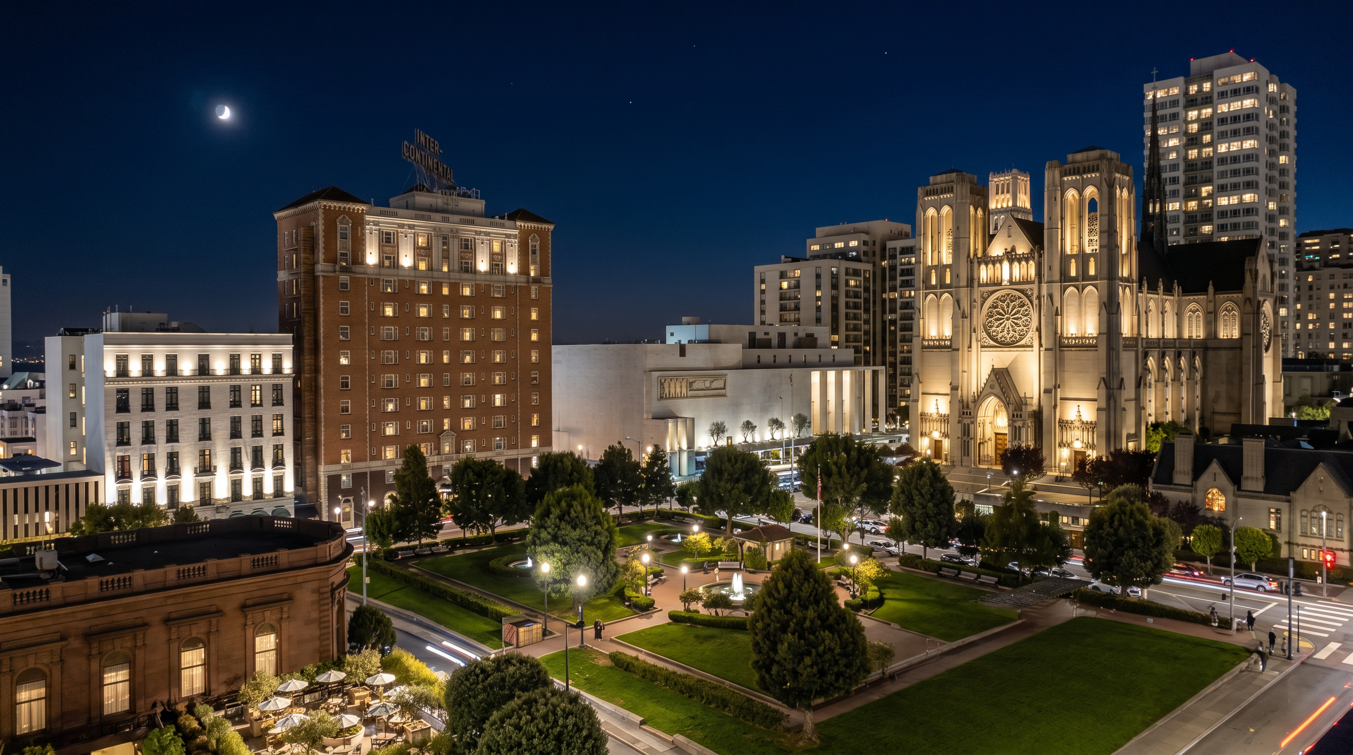 This high-angle aerial view captures a vibrant urban park surrounded by historic architecture, including a prominent cathedral and classic brick buildings. The scene features well-manicured green lawns, mature trees, and paved walkways, with a foreground terrace offering outdoor seating. The perspective provides a comprehensive look at the neighborhood's layout and its integration with the surrounding city landscape.
