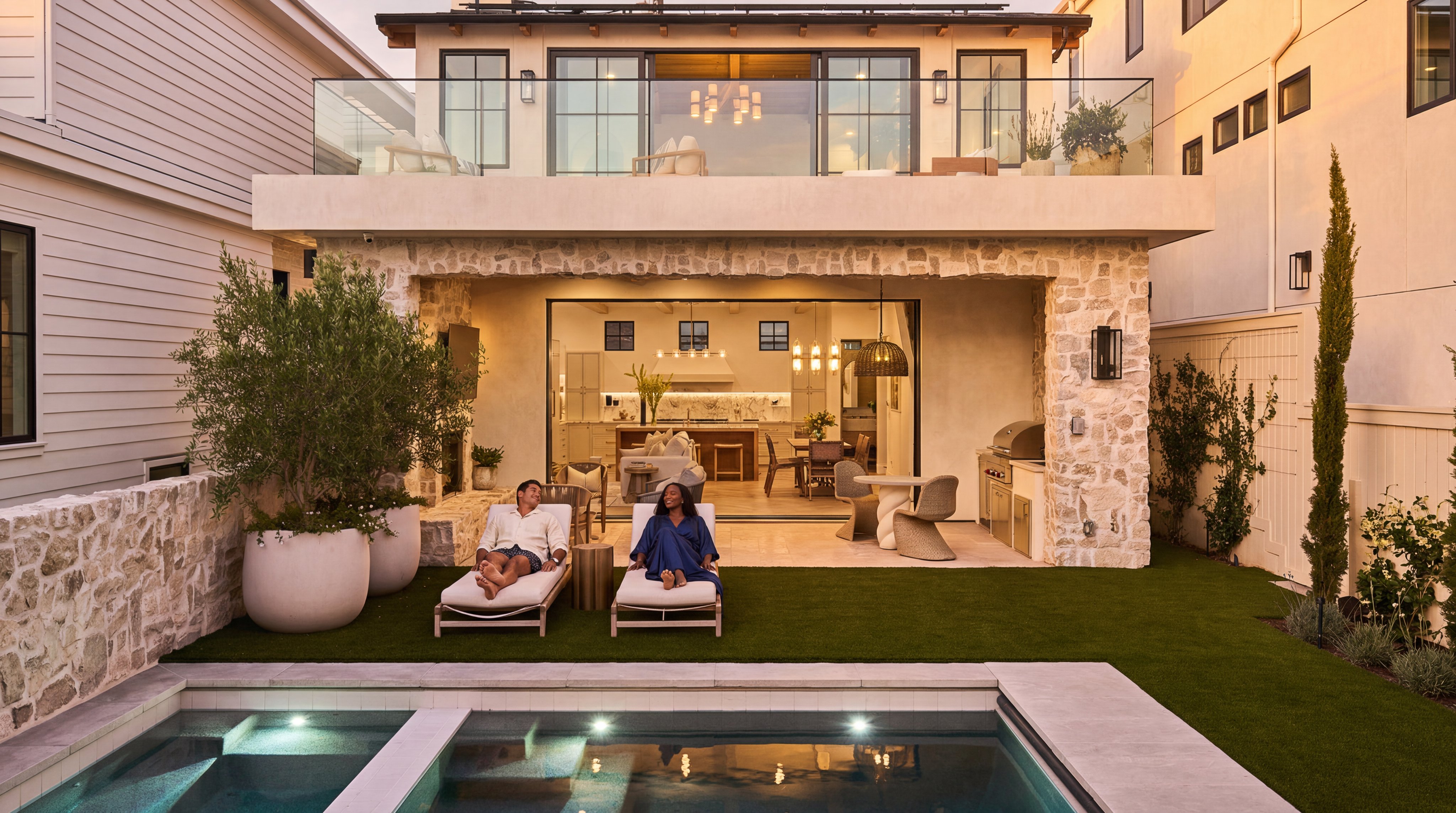 This stunning contemporary residence features a seamless indoor-outdoor transition, leading from an open-concept interior to a spacious covered patio. The rear exterior boasts natural stone cladding, a tiered balcony with glass railings, a private swimming pool, and manicured green space, creating an ideal setting for luxury relaxation. The balanced architectural design highlights both elegant modern finishes and warm, inviting outdoor living areas.