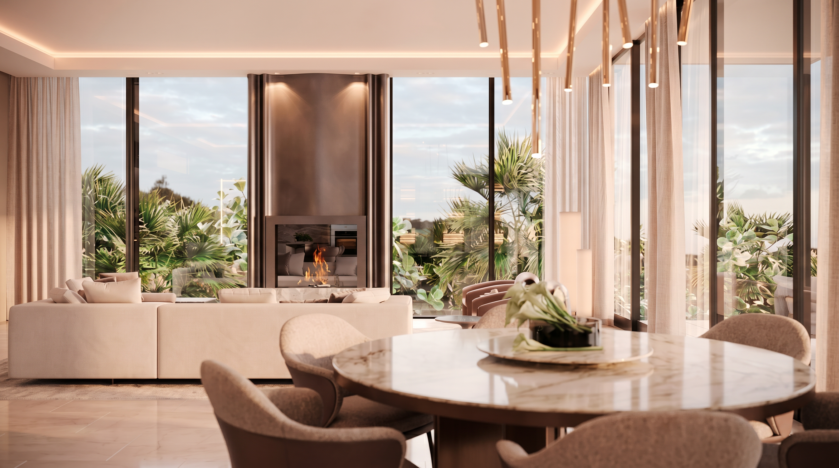 This sophisticated open-concept living and dining area features a neutral color palette and a seamless connection to the outdoors through expansive glass walls. A prominent, tall metallic fireplace surround serves as a central focal point, while a circular stone-topped dining table and plush seating create an inviting atmosphere. The space is illuminated by elegant, slender pendant lighting, offering a luxurious and modern aesthetic with lush greenery visible outside.