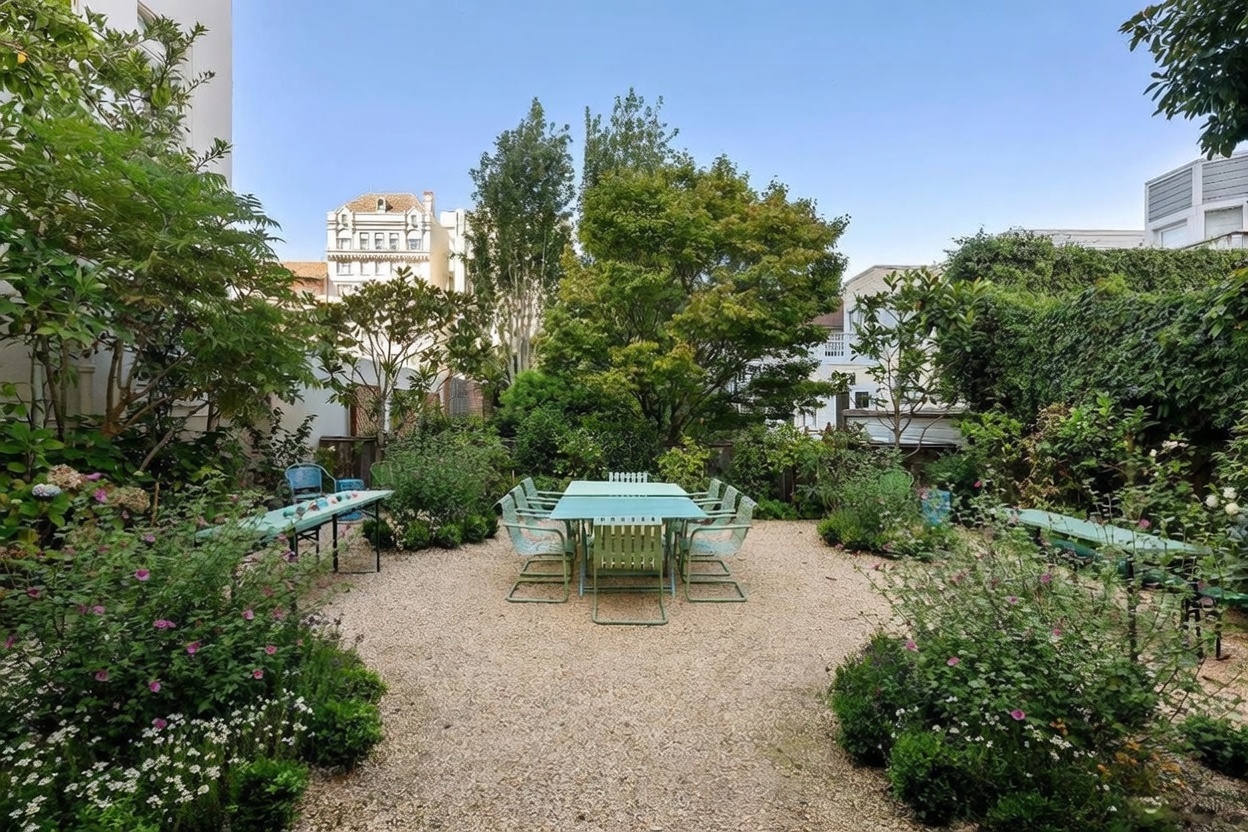 This serene, private garden features a central gravel courtyard furnished with a metal dining set, surrounded by lush greenery and mature trees. The space is framed by flowering shrubs and climbing vines, creating a peaceful outdoor retreat. The perspective is a wide, eye-level shot that captures the depth and tranquil atmosphere of the backyard.