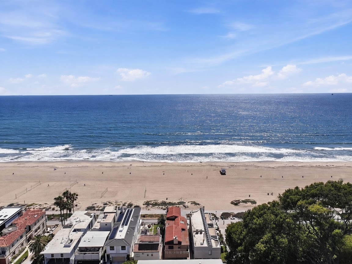 This high-angle aerial view captures a prime beachfront location, showcasing the expansive sandy beach and the vast, shimmering ocean horizon. In the foreground, several residential properties are visible, highlighting their immediate proximity to the coastline and the coastal lifestyle. The perspective provides a clear sense of the property's location relative to the water, emphasizing the unobstructed ocean views.