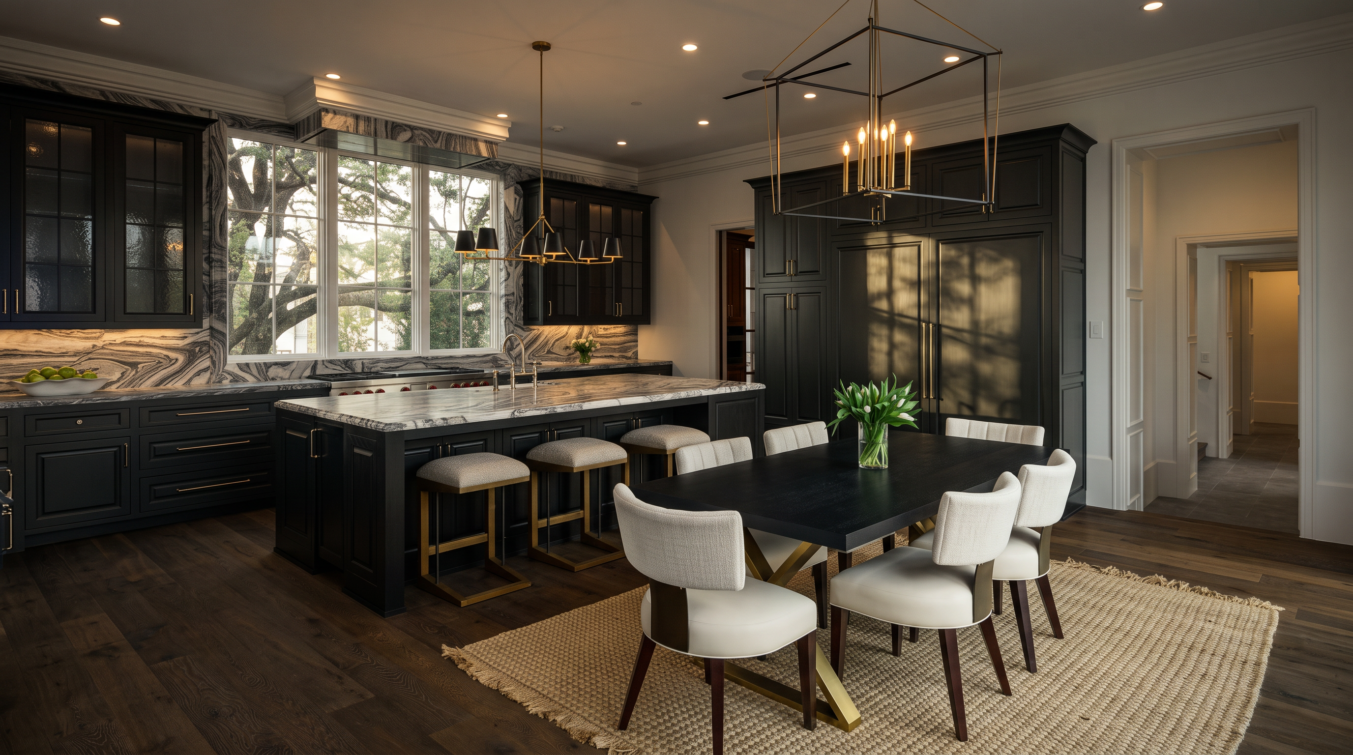 This sophisticated kitchen features dark cabinetry paired with striking, heavily veined stone countertops and backsplashes. A large central island provides seating for three, while an adjacent dining area is anchored by a dark wood table and upholstered chairs set upon a textured rug. The space is illuminated by modern geometric pendant lighting and large windows that offer a view of mature trees outside.