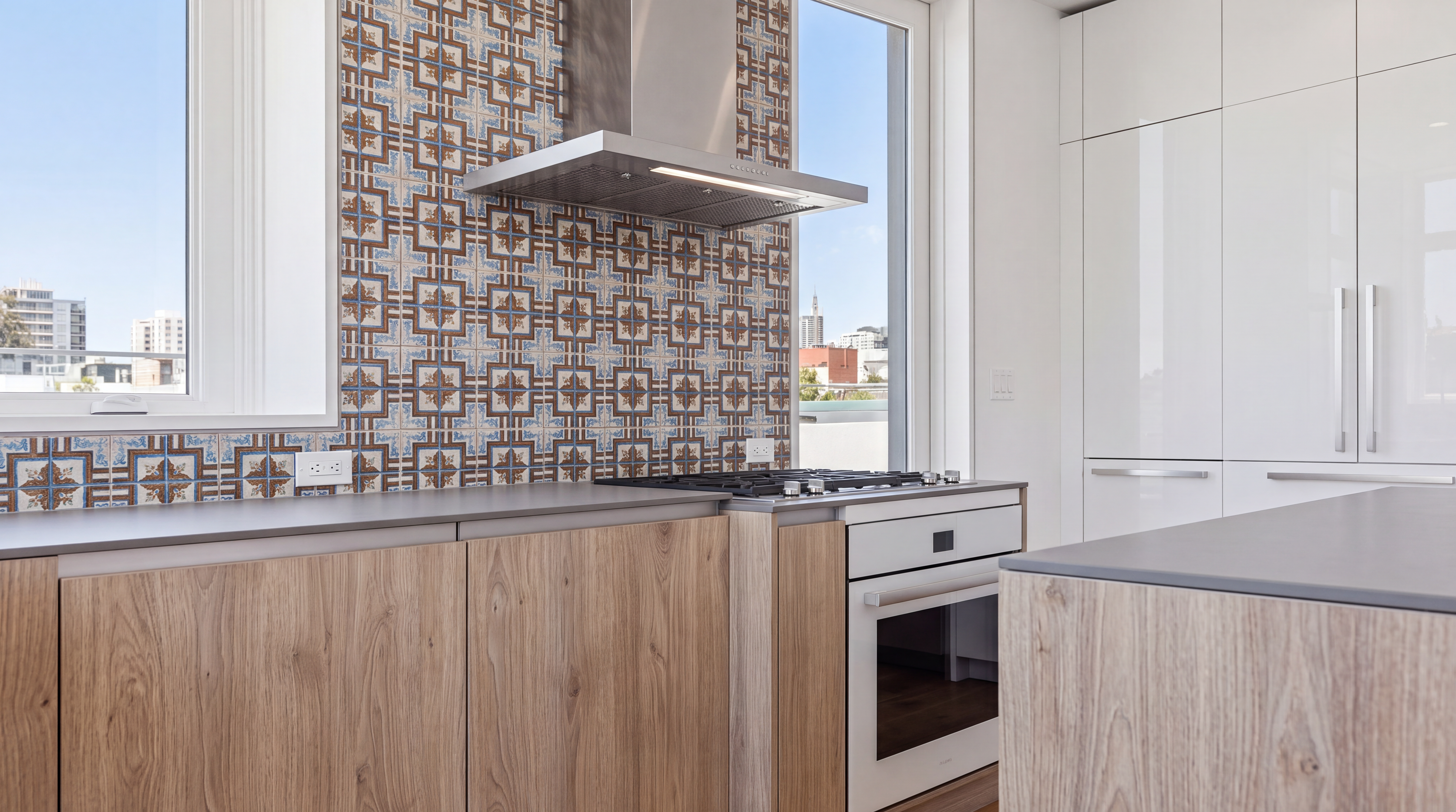 This sleek, modern kitchen features natural wood cabinetry paired with contemporary matte gray countertops and minimalist white high-gloss pantry doors. A striking decorative patterned tile backsplash serves as a focal point, drawing the eye toward the premium stainless steel range and integrated hood. Large windows on either side of the cooking area provide abundant natural light and panoramic urban views, creating an airy and sophisticated culinary space.