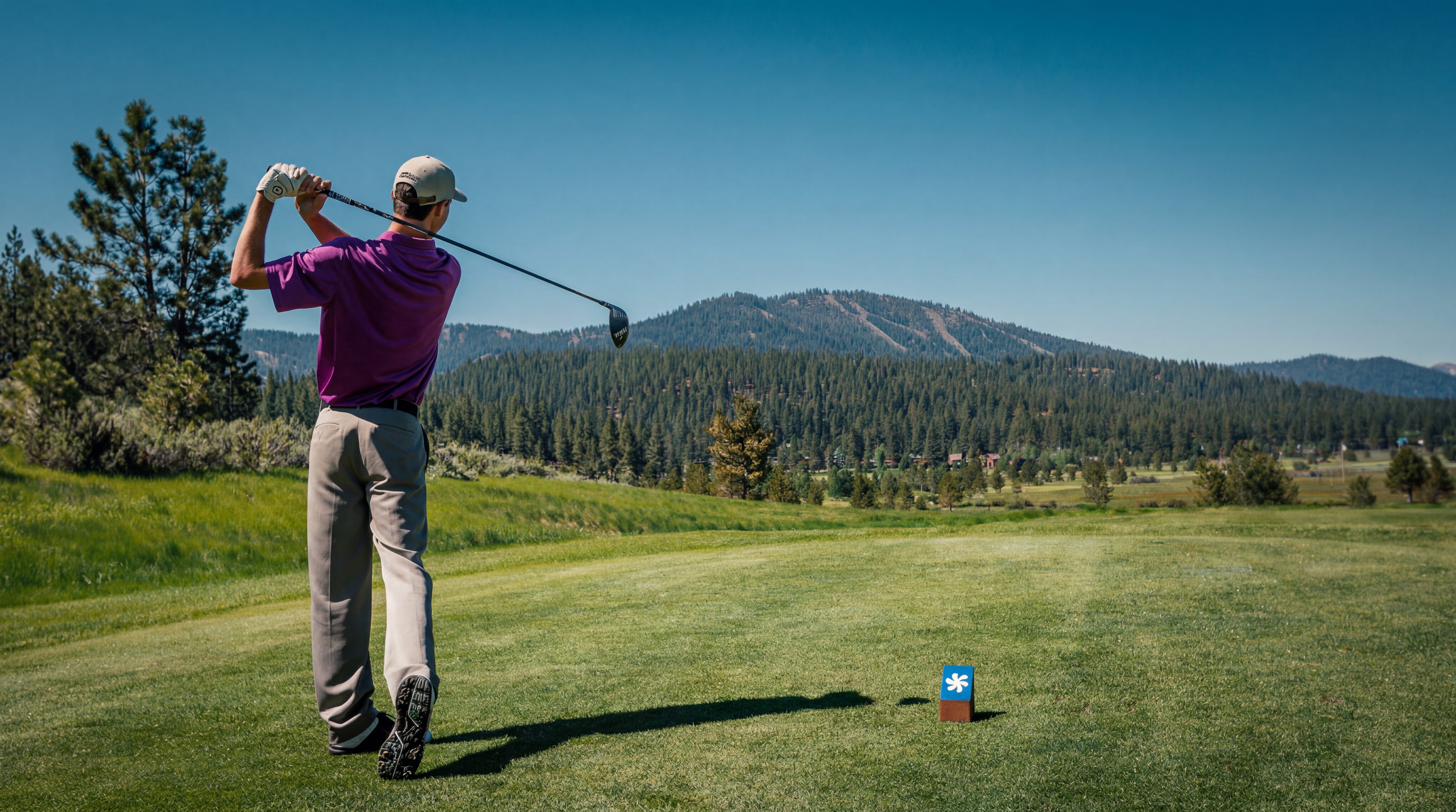 This image captures a golf course tee box area, showcasing a well-manicured fairway set against a scenic backdrop of pine-forested mountains. A feature like this adds significant recreational value to a residential community, highlighting access to outdoor leisure activities. The vast, open landscape and natural beauty convey a desirable, active lifestyle setting.