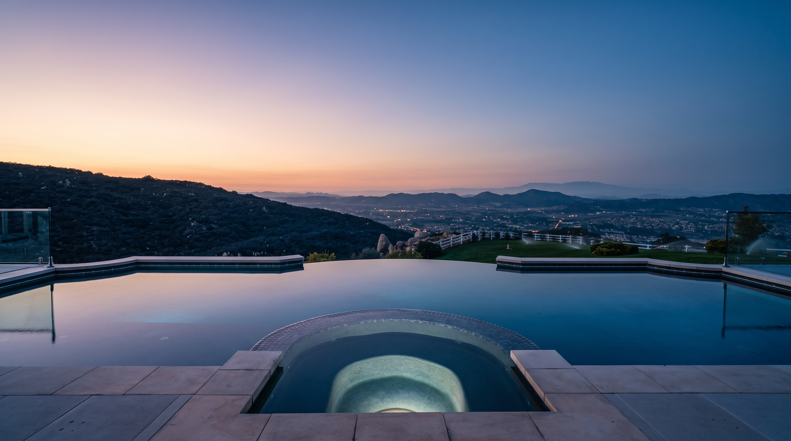 This stunning infinity-edge pool and integrated spa offer breathtaking panoramic views of the valley below and distant mountains at sunset. The sleek design features modern tiling and clean stone coping, seamlessly blending luxury water elements with the surrounding natural landscape. The meticulously maintained backyard, complete with a sprawling green lawn and scenic vista, creates an ideal setting for high-end outdoor entertaining.