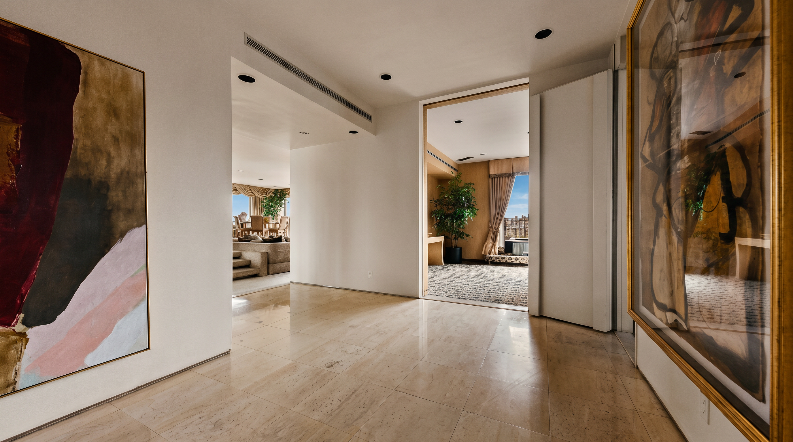 This bright, expansive foyer features polished light-toned stone flooring and minimalist white walls adorned with large, abstract art pieces. The perspective looks through a wide, open doorway into a secondary living space, creating a sense of depth and flow between rooms. Recessed lighting is integrated into the ceiling, contributing to the clean, sophisticated aesthetic of this high-end interior.