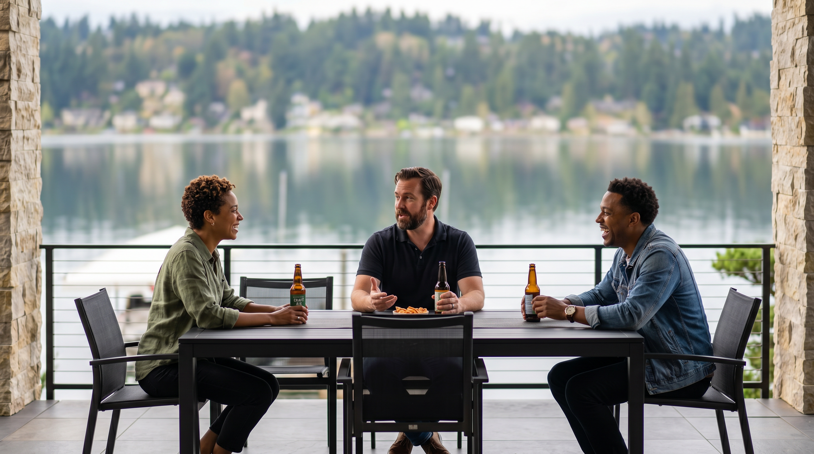 This covered outdoor patio features a large dining table with six chairs, framed by two substantial stone-clad pillars and a wide arched ceiling. The space offers an expansive, unobstructed view of a calm lake and a distant, tree-lined shoreline under a clear blue sky. The sleek, modern design is complemented by a minimalist metal railing, creating a sophisticated and serene atmosphere for outdoor entertaining.