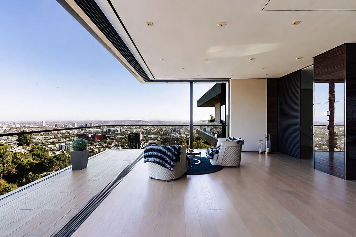 This luxurious, modern balcony offers an expansive, unobstructed panoramic view of the city skyline, seamlessly blending indoor and outdoor living through floor-to-ceiling glass walls. The space is furnished with two elegant, textured armchairs arranged on a dark circular rug, creating a sophisticated lounge area on the light hardwood deck. The clean lines and minimalist aesthetic emphasize the breathtaking vista, making it an ideal setting for high-end relaxation.
