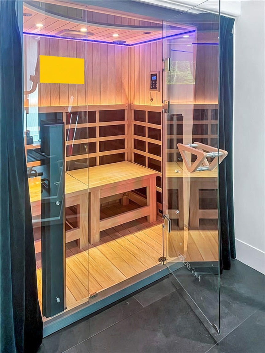 This image showcases a modern, high-end infrared sauna with light wood paneling and integrated bench seating. The structure features a glass door with a distinctive wooden handle and is framed by dark curtains, creating a sleek and wellness-focused aesthetic. The interior is illuminated by soft, ambient lighting, highlighting the clean lines and contemporary design of this home spa feature.