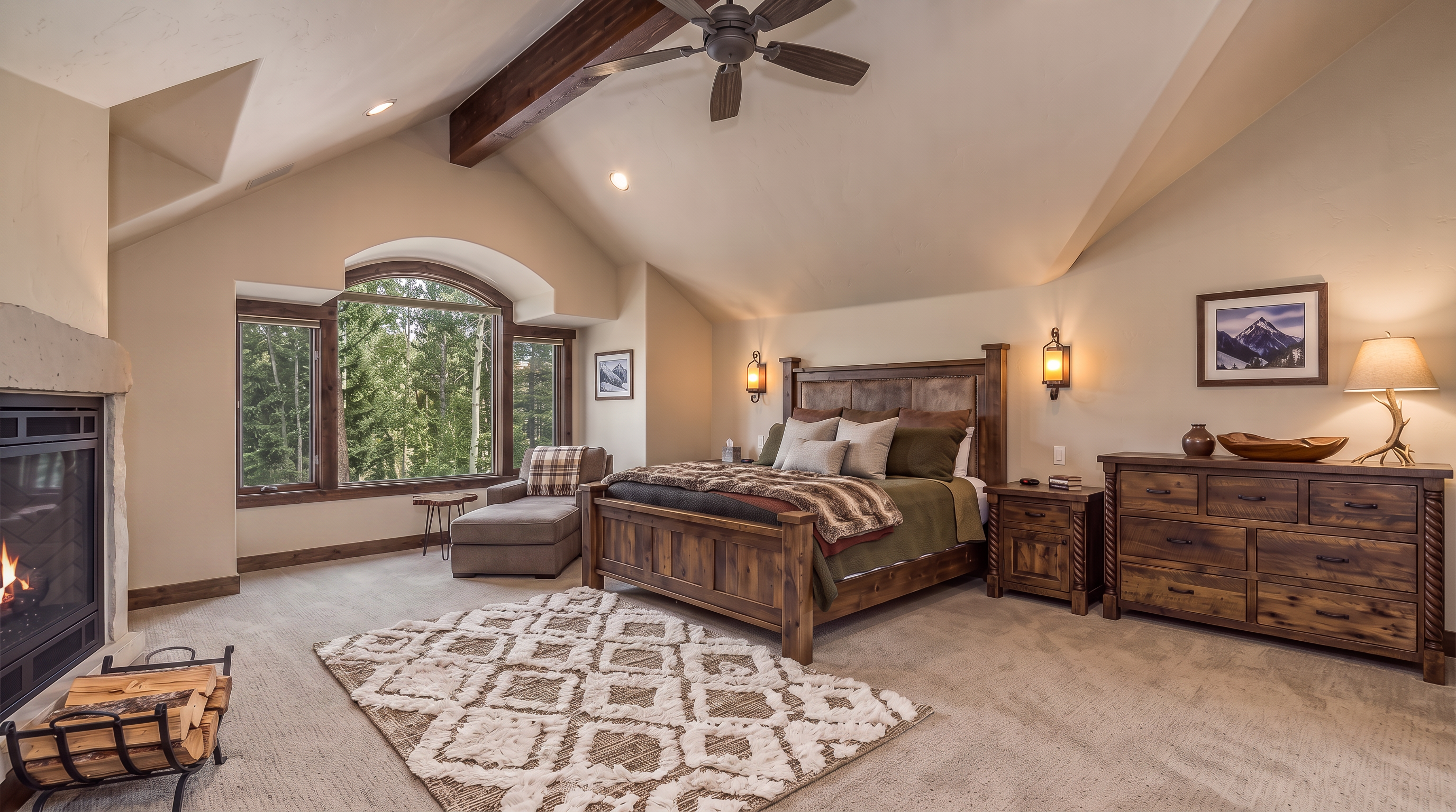 This cozy, mountain-style primary bedroom features vaulted ceilings with exposed wood beams and a large arched window overlooking a forested view. The room is well-appointed with a rustic wooden bed frame, a leather armchair by the stone fireplace, and a matching wood dresser, creating a warm and inviting atmosphere. A plush area rug over neutral carpeting adds comfort to the space, which is accented by tasteful lighting and nature-inspired decor.