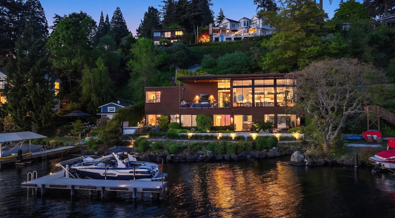 This stunning waterfront property is captured at dusk, showcasing a contemporary multi-level home with warm interior lighting glowing through expansive glass walls. The residence features a spacious deck overlooking the lake, a private dock with a boat, and lush landscaping that integrates seamlessly with the natural hillside setting. The cinematic perspective highlights the tranquil atmosphere and the architectural harmony between the modern structure and the surrounding environment.