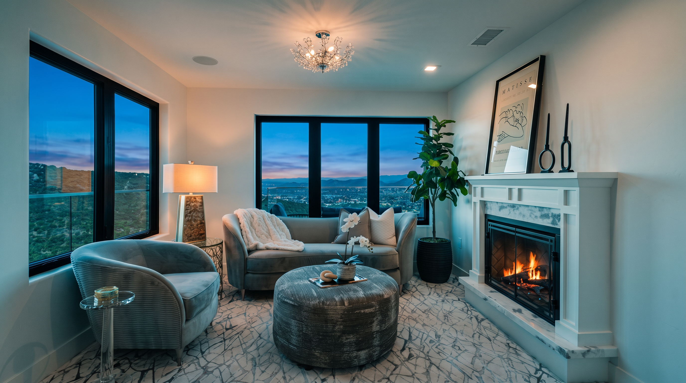 This elegant and serene living room features a sophisticated monochromatic gray color palette, highlighted by a cozy sofa, a tufted round ottoman, and a plush armchair. The space is anchored by a stately white fireplace with a mantel display, while large floor-to-ceiling windows frame breathtaking panoramic views of the surrounding hills. With its refined contemporary style and thoughtful decor, the room offers a luxurious and inviting atmosphere perfect for relaxation.