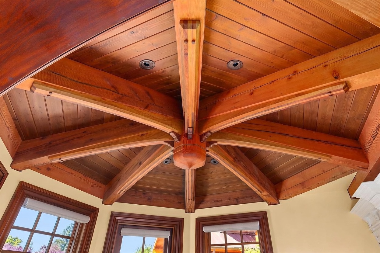 This image captures a striking vaulted ceiling featuring a complex radial timber beam structure that converges at a central wooden pendant. The warm-toned wood planks and exposed beams create a rustic, artisanal aesthetic, while recessed lighting is integrated into the ceiling panels. The perspective is looking directly upward, emphasizing the intricate craftsmanship and geometric symmetry of the architectural design.