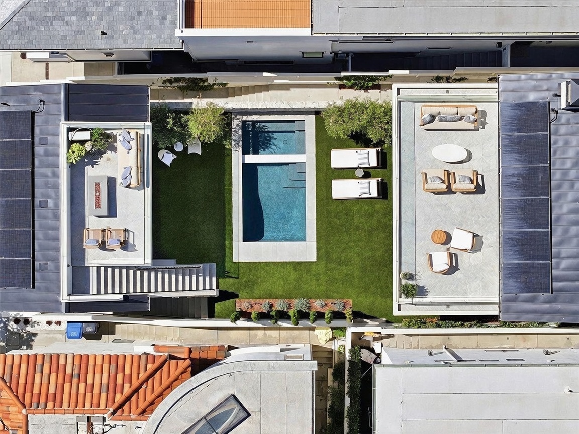 This high-angle aerial view captures a modern, meticulously landscaped backyard featuring a rectangular swimming pool centered between two distinct patio areas. The space includes artificial turf, lounge seating, and a fire pit area, all arranged to create a seamless indoor-outdoor living experience. The clean lines and contemporary design elements highlight a sophisticated and private urban oasis.