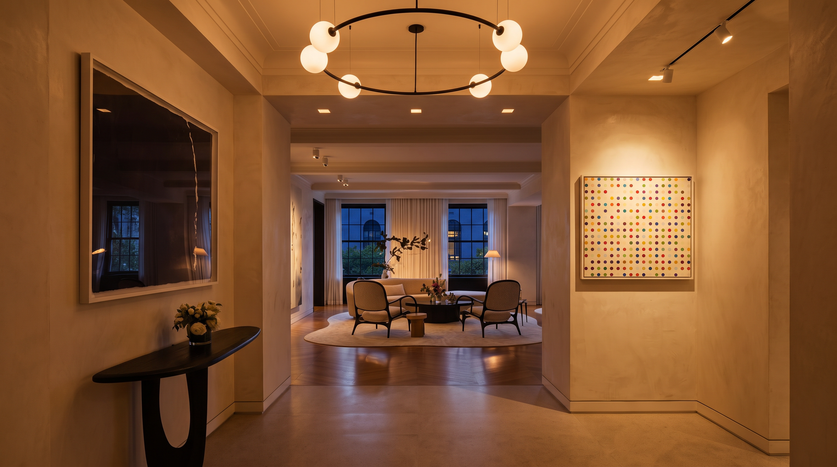 This gallery-like entryway leads into a sophisticated open-concept living area, showcasing a blend of contemporary art and elegant furnishings. The space is anchored by a striking custom circular chandelier and high-end finishes, creating a luxurious and welcoming atmosphere. The neutral color palette, polished flooring, and curated decor emphasize the home's refined and timeless design.